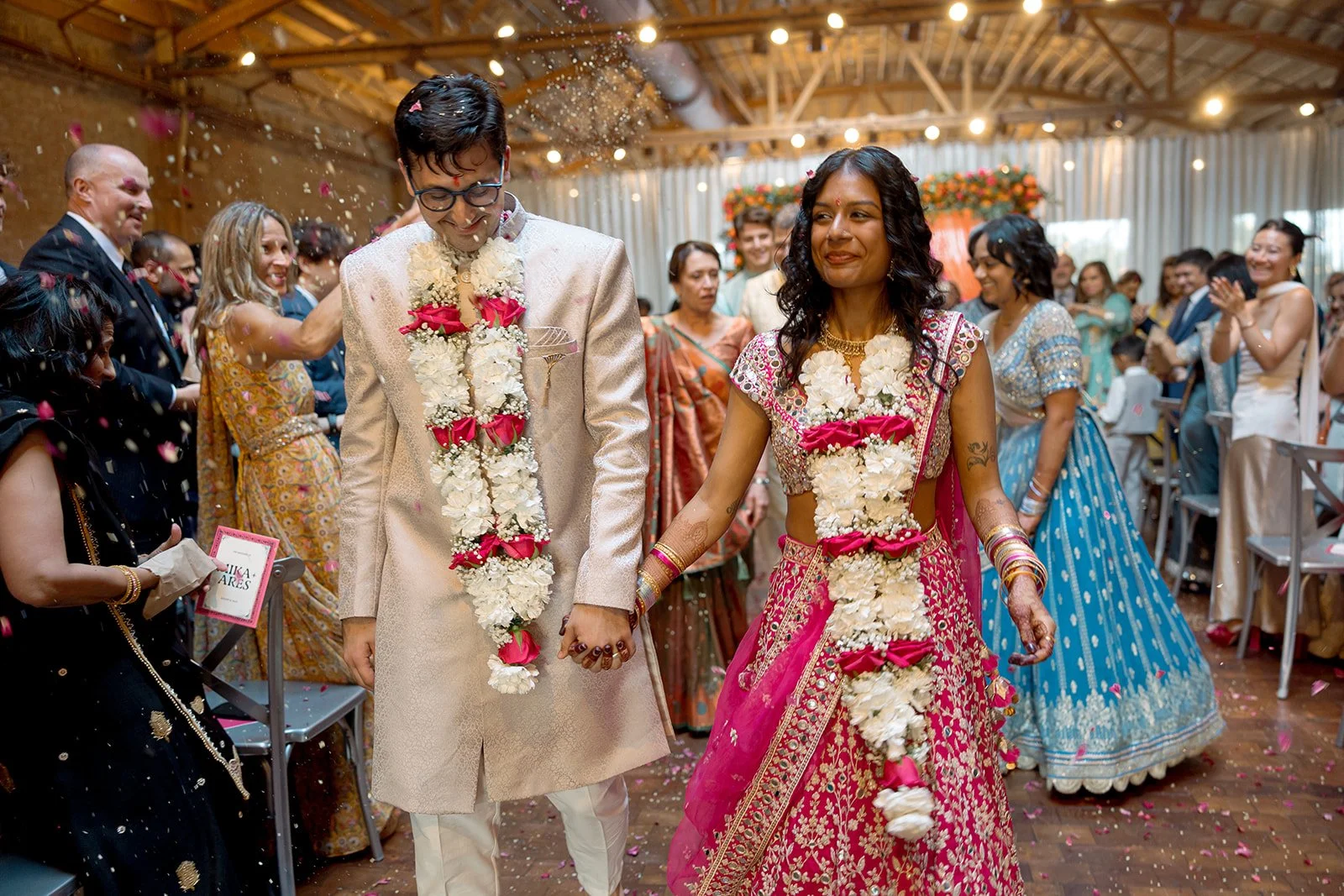 Bride in a pink lehenga and groom in a sherwani walking the recessional amid confetti at an Indian wedding ceremony at Rockwell on the River in Chicago, photographed by Louie Abellera.