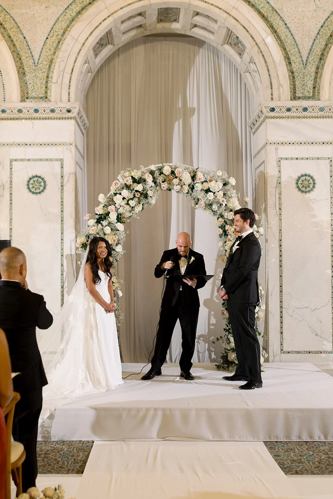 Sarah and Brennan stand under a stunning white floral arch during their ceremony at Chicago Cultural Center. Shot on film by a Chicago wedding photographer.