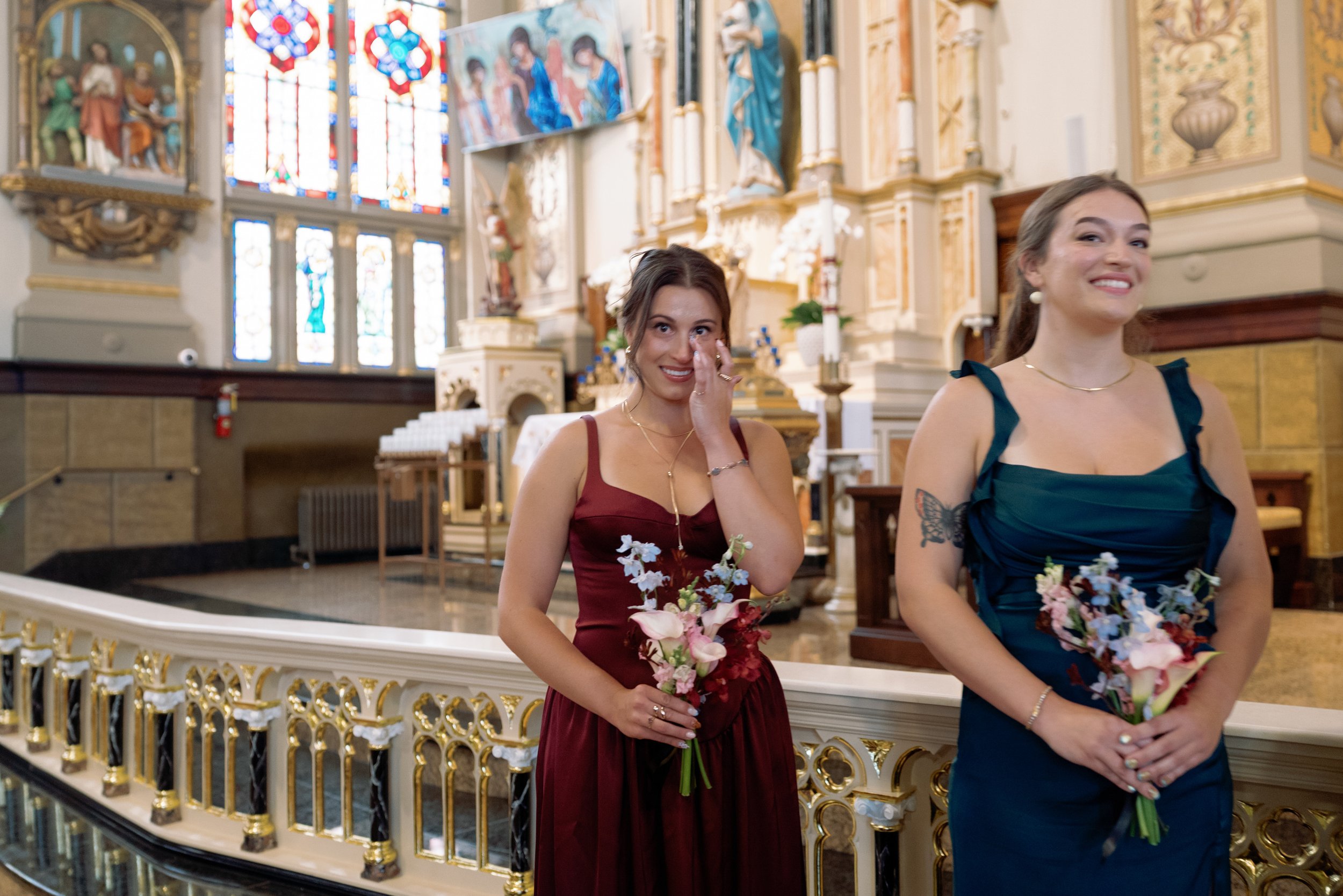 Bridesmaids share an emotional moment in the church balcony, one wiping away tears