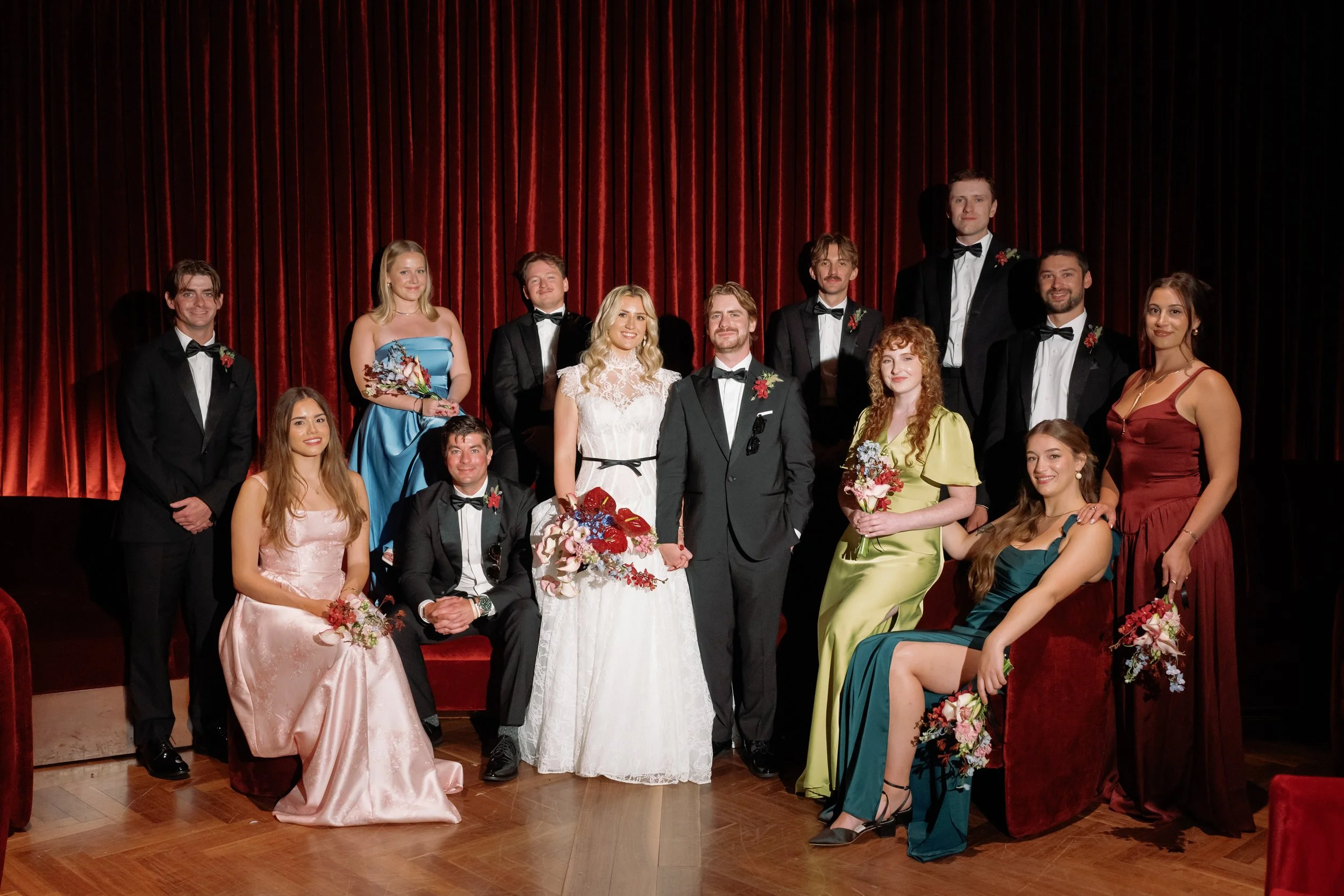 Full wedding party formal portrait on the stage inside The Wellsley's red velvet lounge