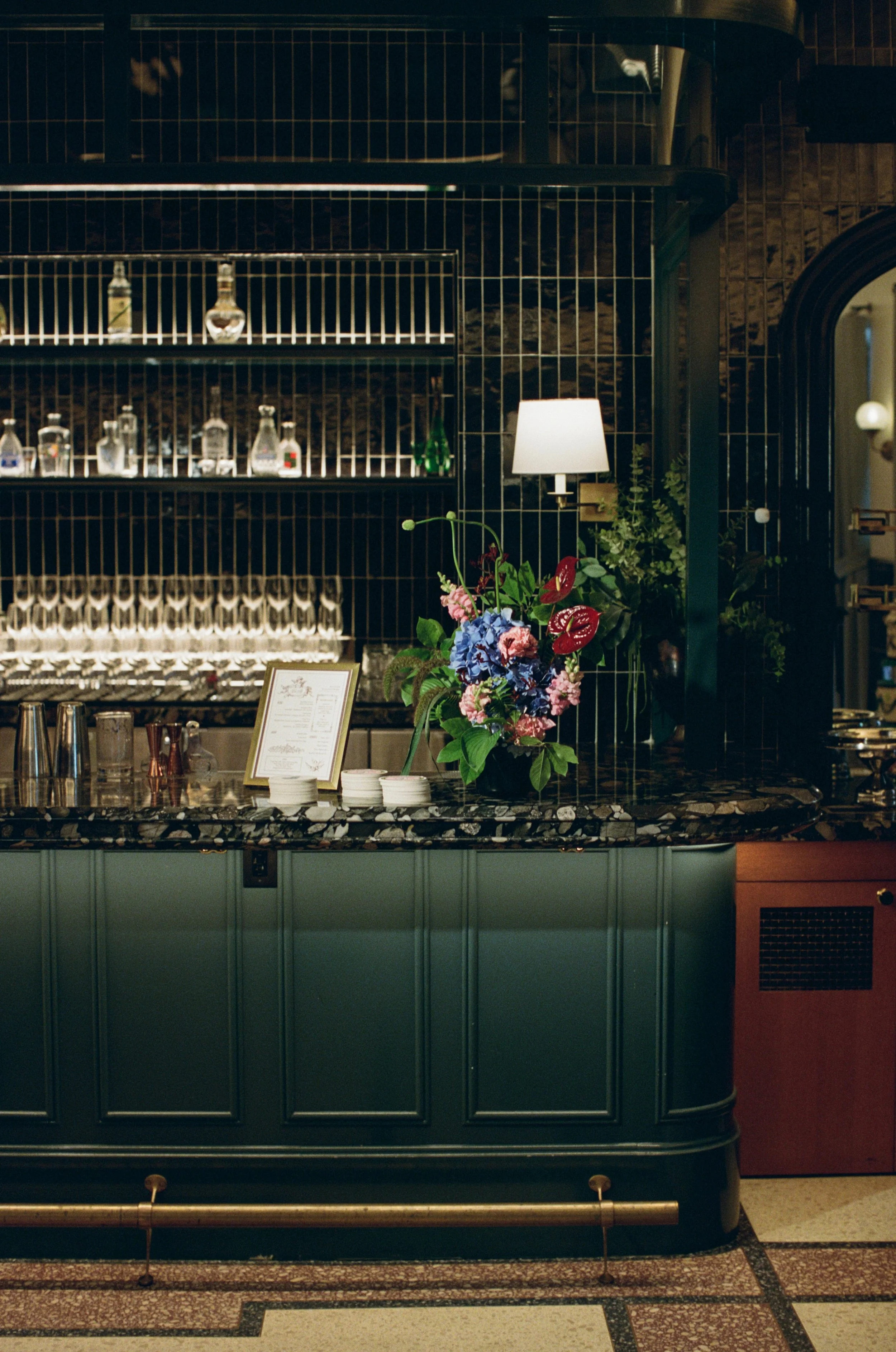 Floral arrangement styled on a teal bar counter beneath a brass wall sconce