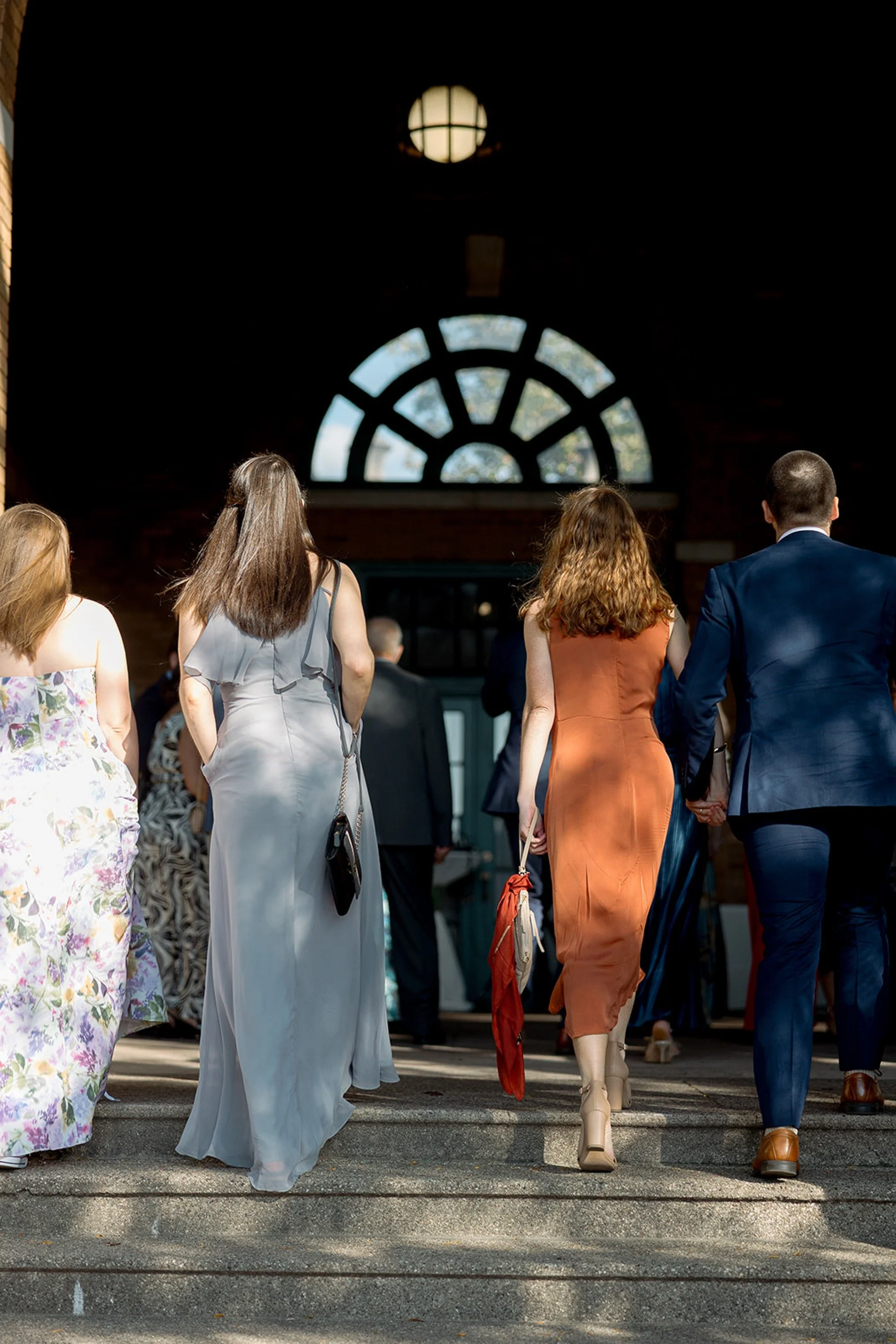 Guests climb the broad steps and disappear through the grand arched entrance of Columbus Park Refectory — backlit, colorful, and full of anticipation. A quietly striking arrival shot