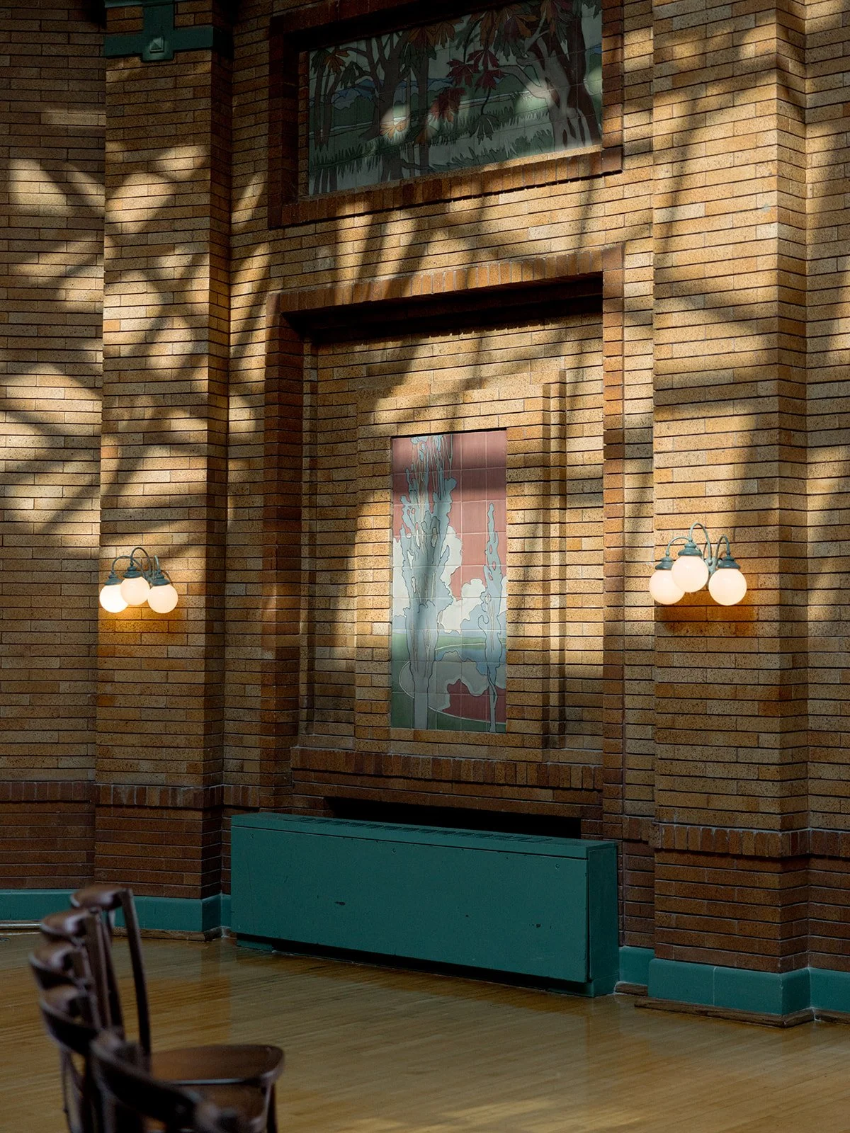 Dappled afternoon light on Cafe Brauer's Great Hall — original tile mural, signature teal trim, and ornate wall sconces.