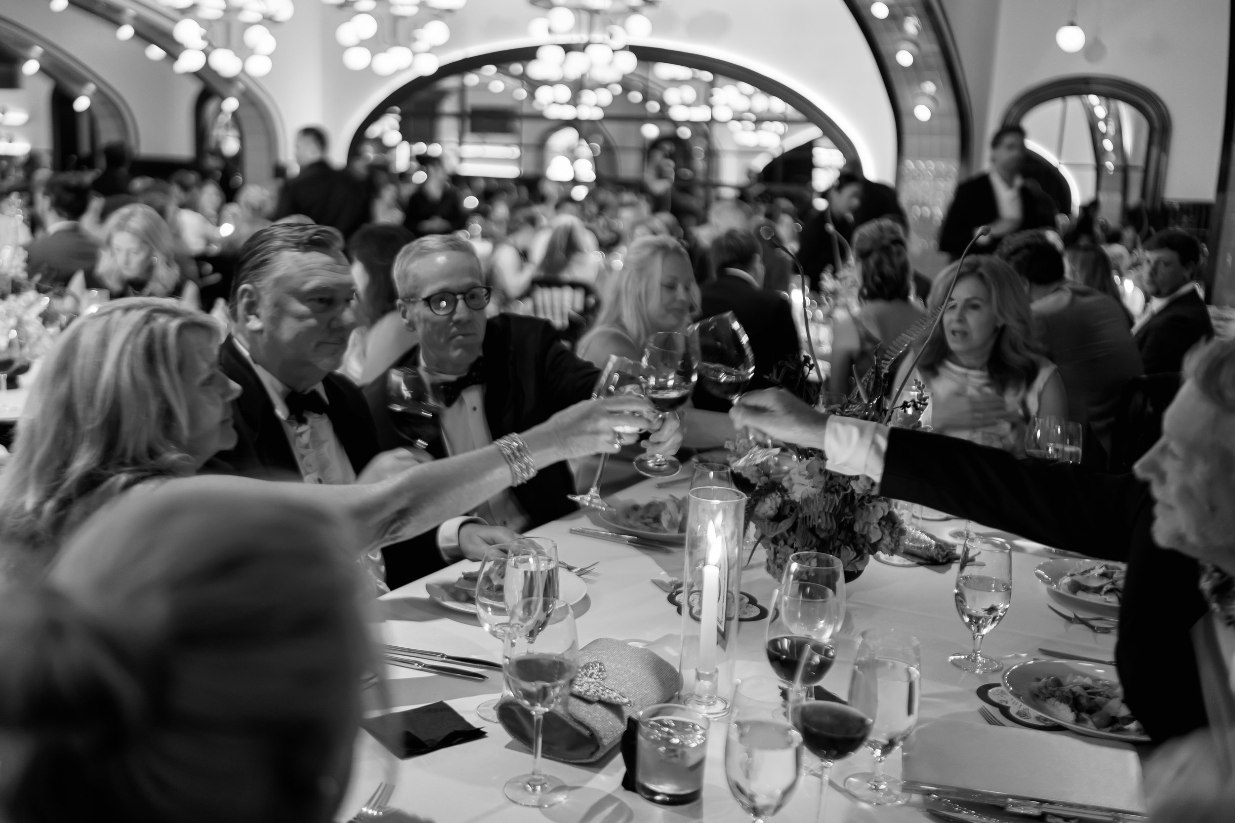 Black and white photo of guests clinking glasses in a toast at the reception
