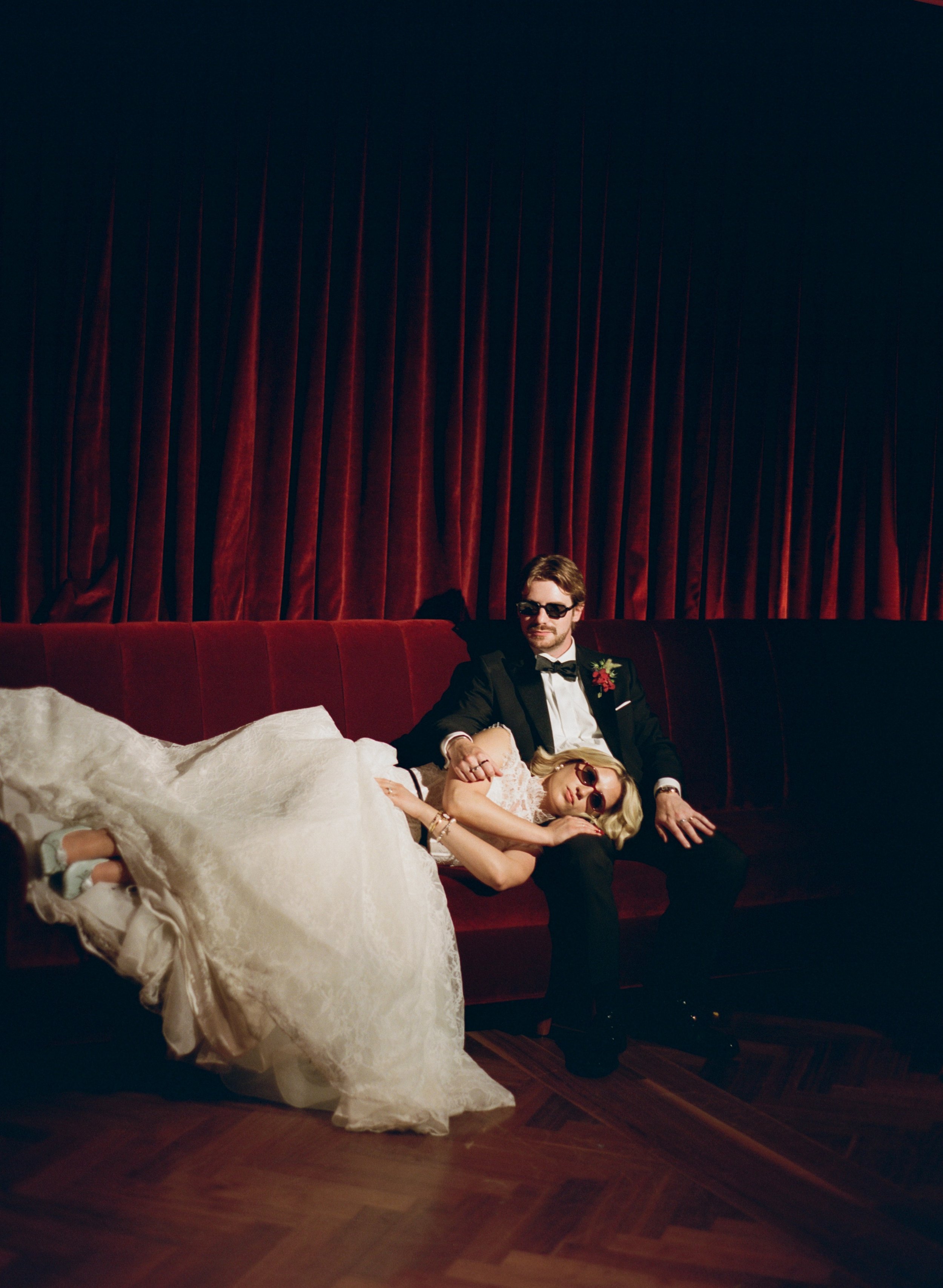 Bride playfully reclines across the groom's lap on a velvet couch in The Wellsley's red velvet lounge