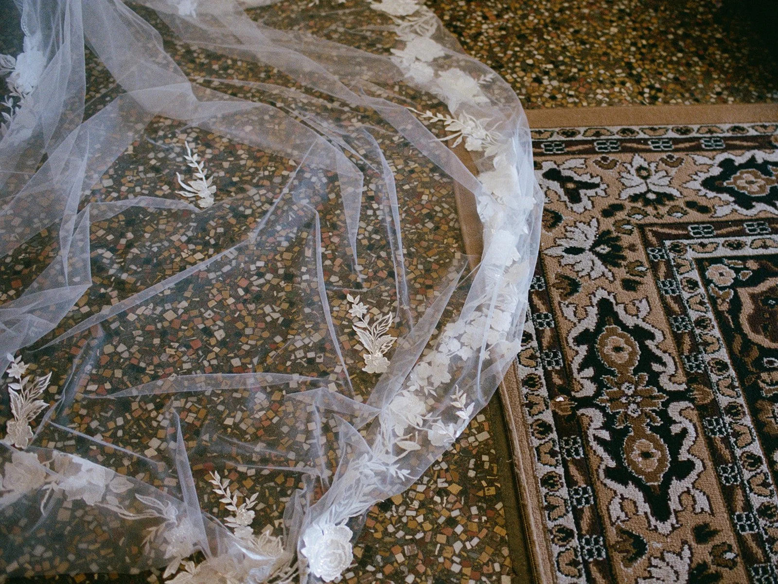 A stunning detail of the bride's cathedral veil and delicate lace train, draped on oriental carpet in the getting ready suite. Shot on film by a Chicago film wedding photographer.