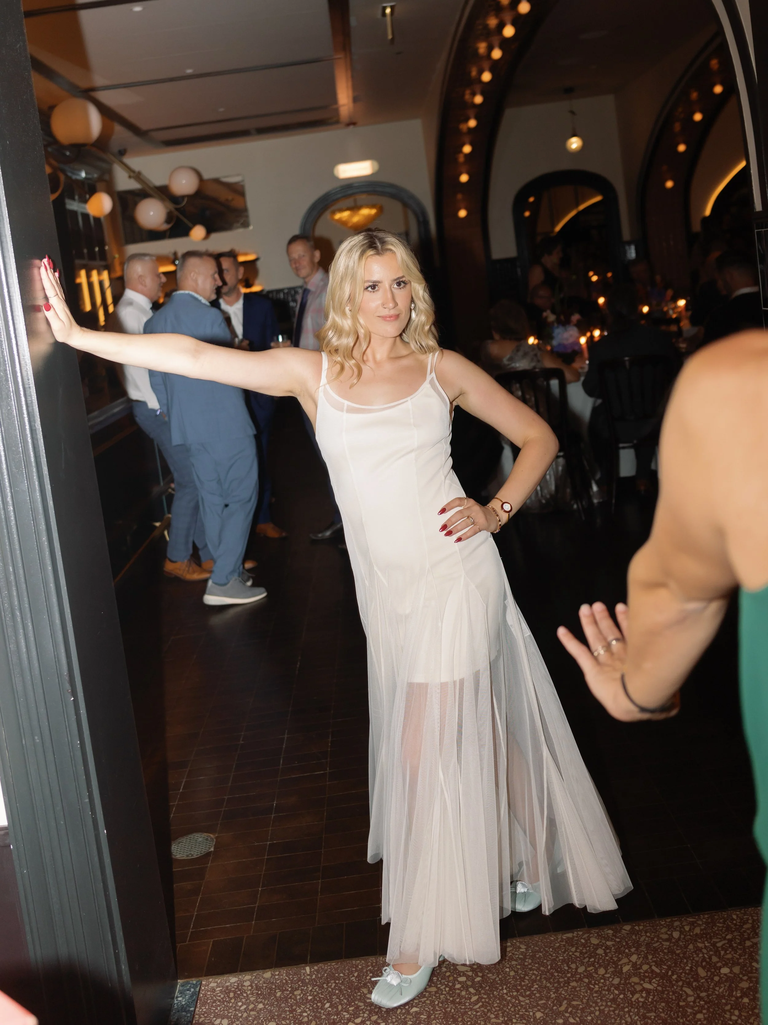 Bride dances in a sheer slip dress at the afterparty, one hand braced on the doorway