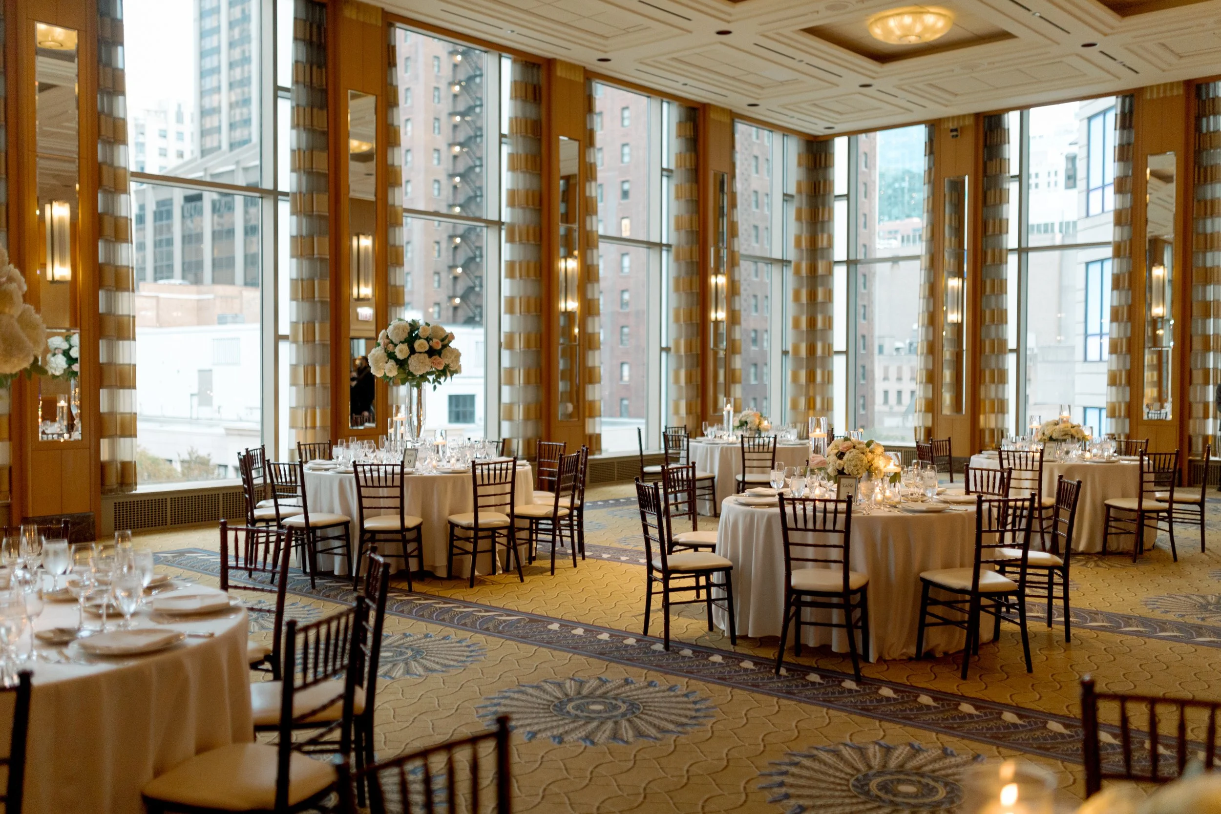 Peninsula Chicago reception hall in daylight with round tables, chiavari chairs and Chicago skyline through tall windows