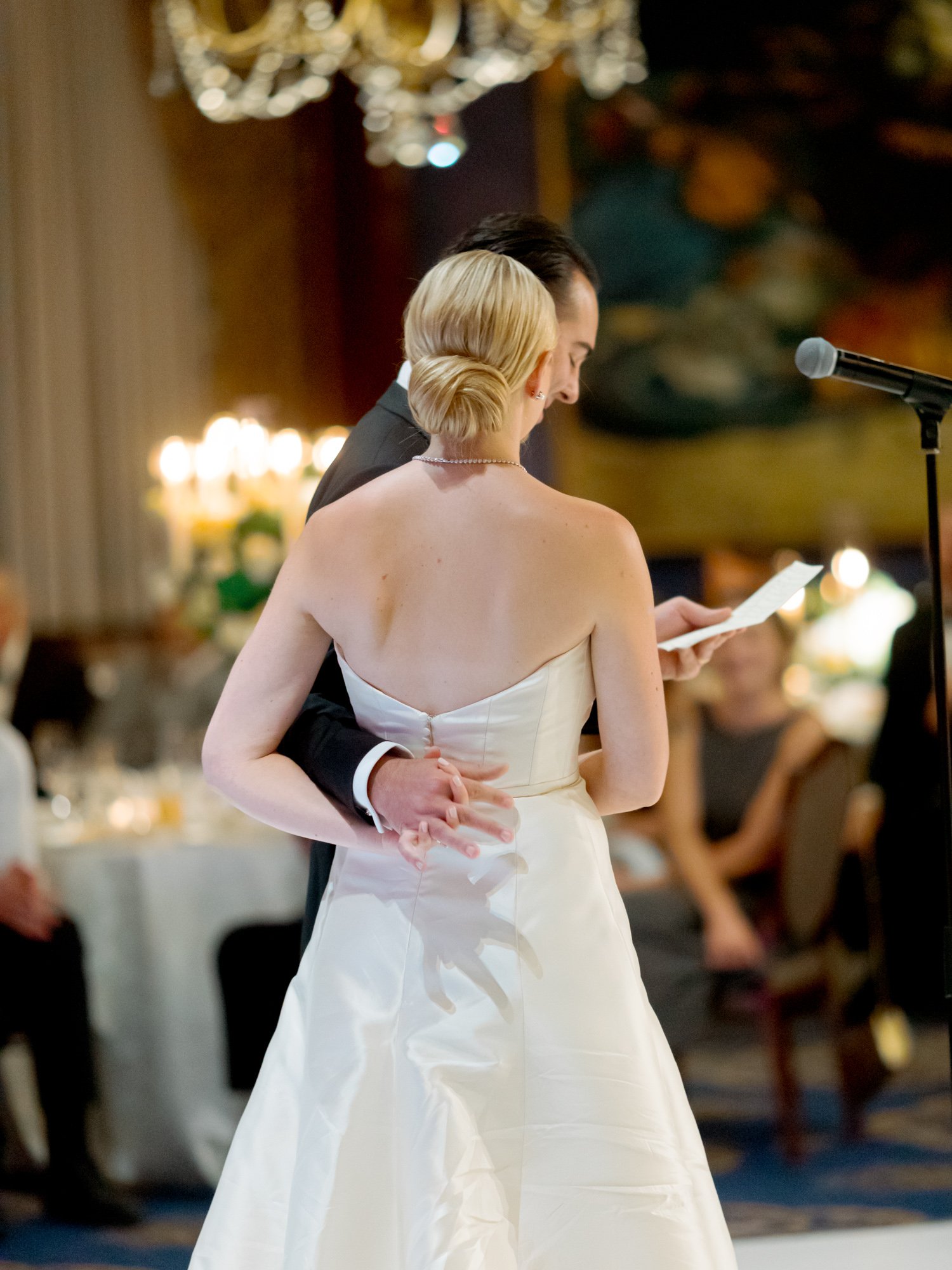 The groom pulls the bride close at her waist during the first dance, candlelit guests looking on from their tables in the Union League Club ballroom.