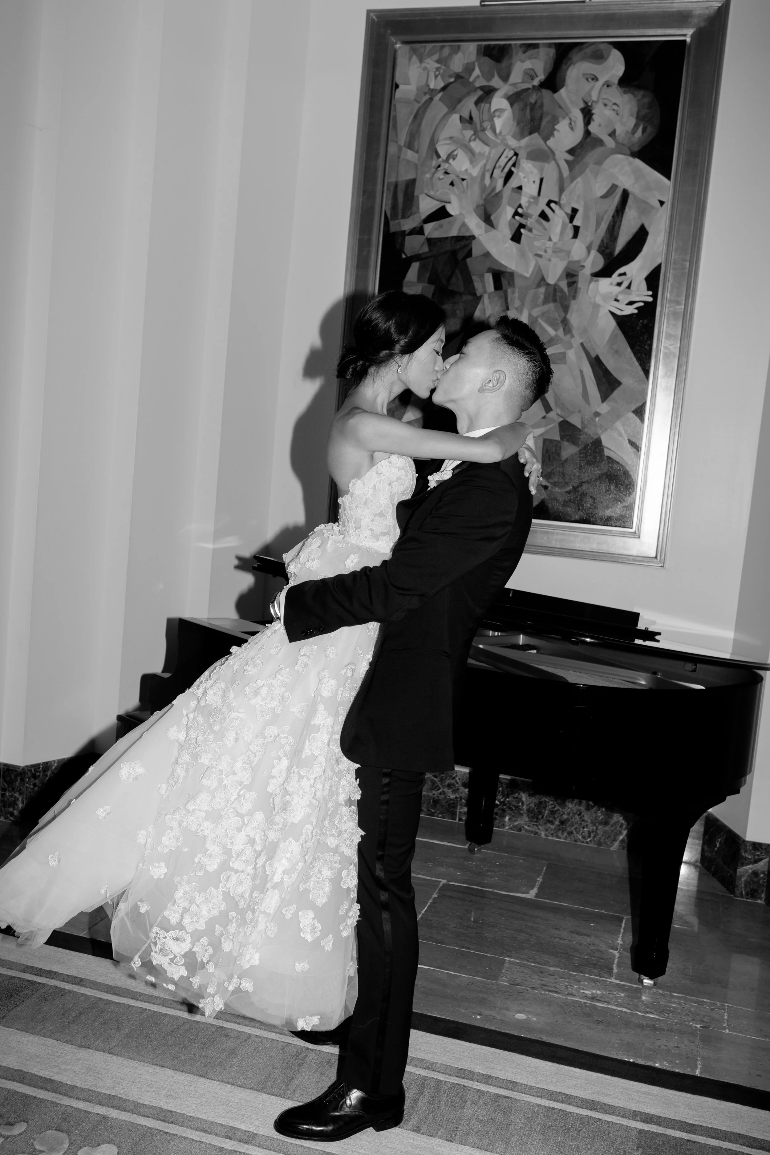 Black and white photo of the groom lifting the bride for a kiss beneath a Cubist painting at The Peninsula Chicago