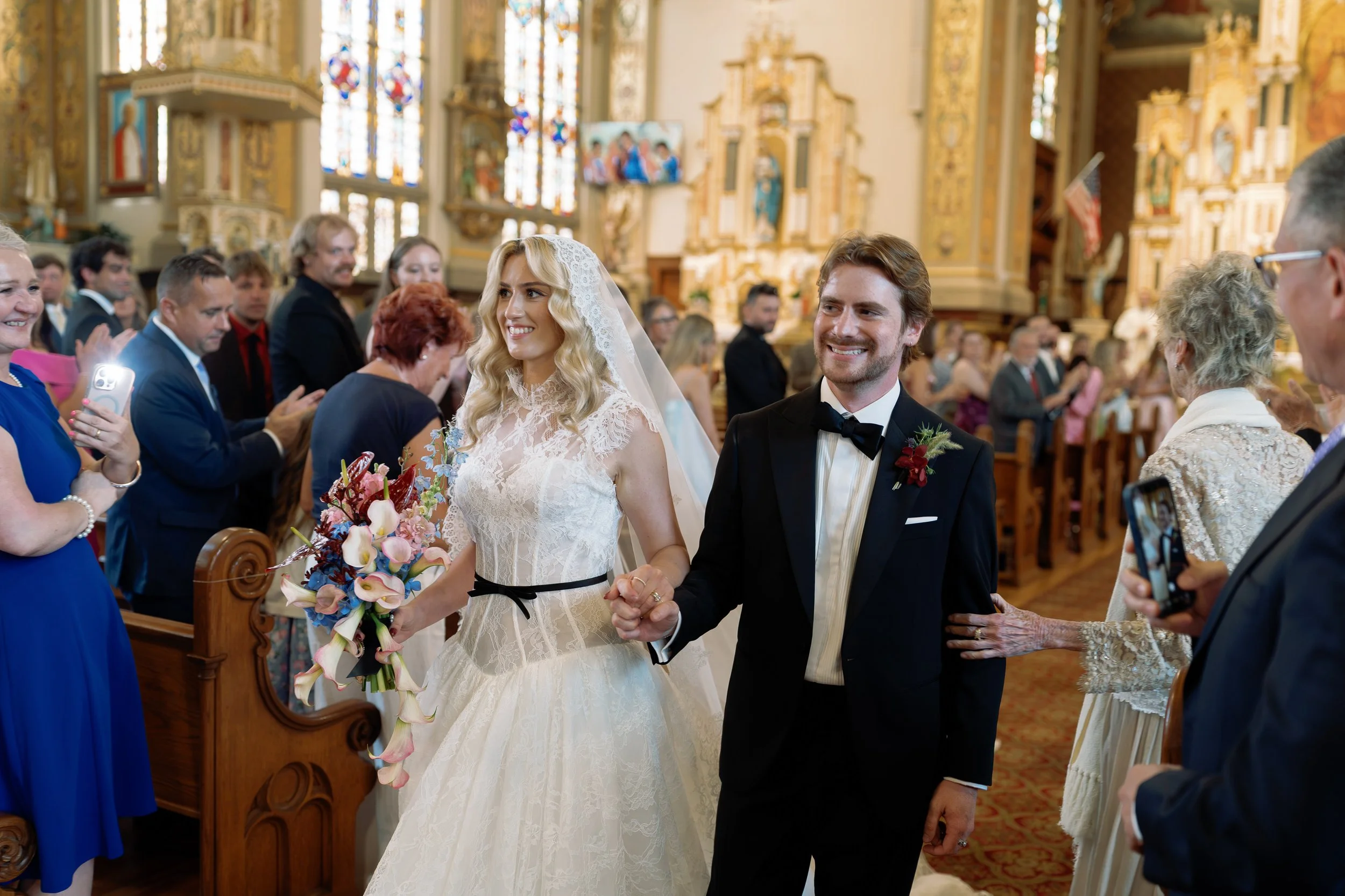 Newlyweds walk down the aisle together, guests smiling, bouquet in hand