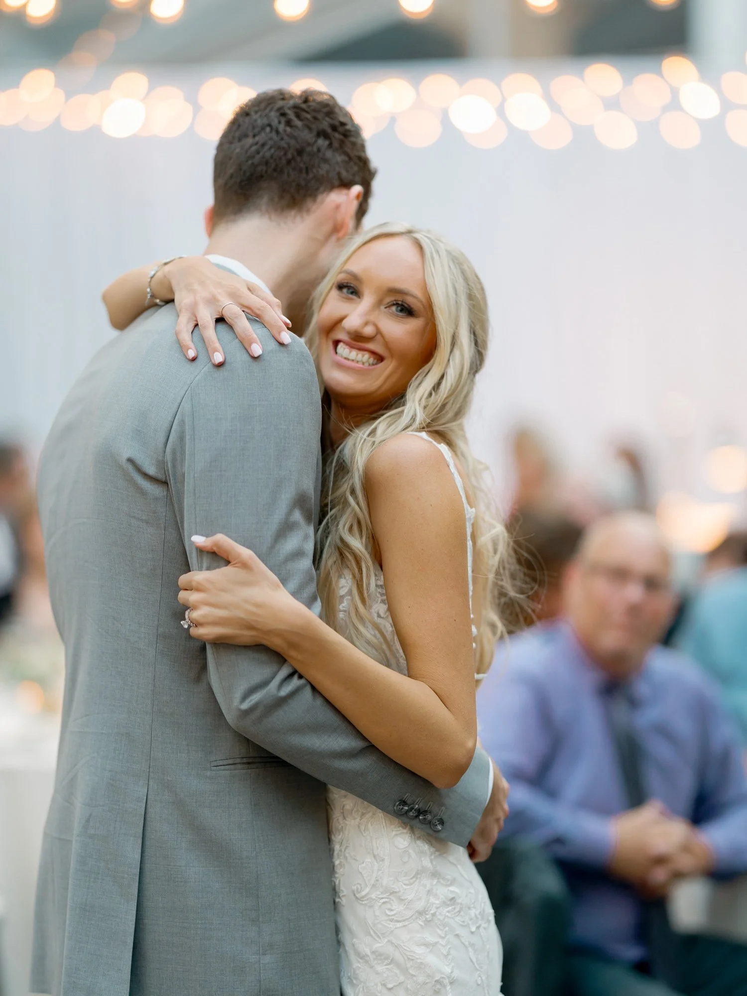 The bride throws her head back with a radiant laugh during the first dance at the Chicago Illuminating Company, globe string lights twinkling above the couple.