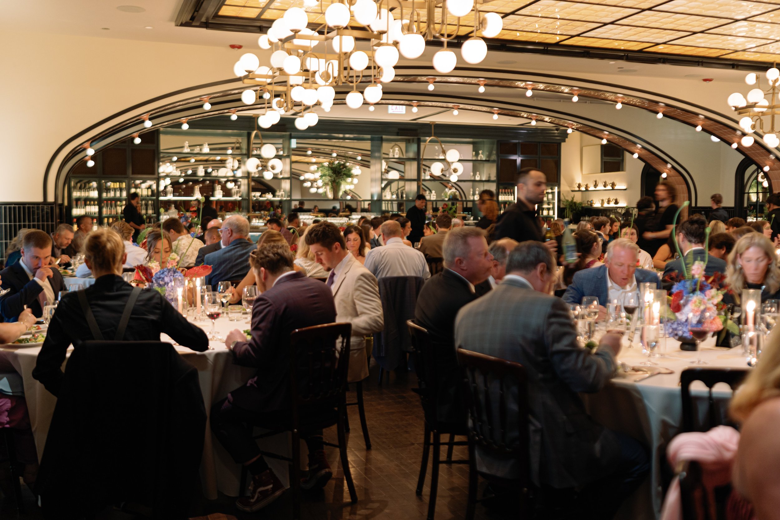 Wide shot of guests seated for dinner beneath the reception room's arched mirrored bar
