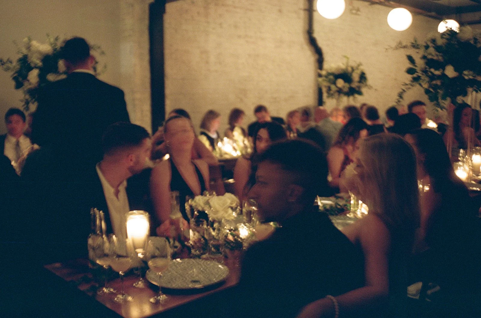 Candid 35mm film photo of wedding guests at candlelit dinner tables inside the warmly lit industrial space at Lytle House in Chicago, photographed by Chicago film wedding photographer Louie Abellera.