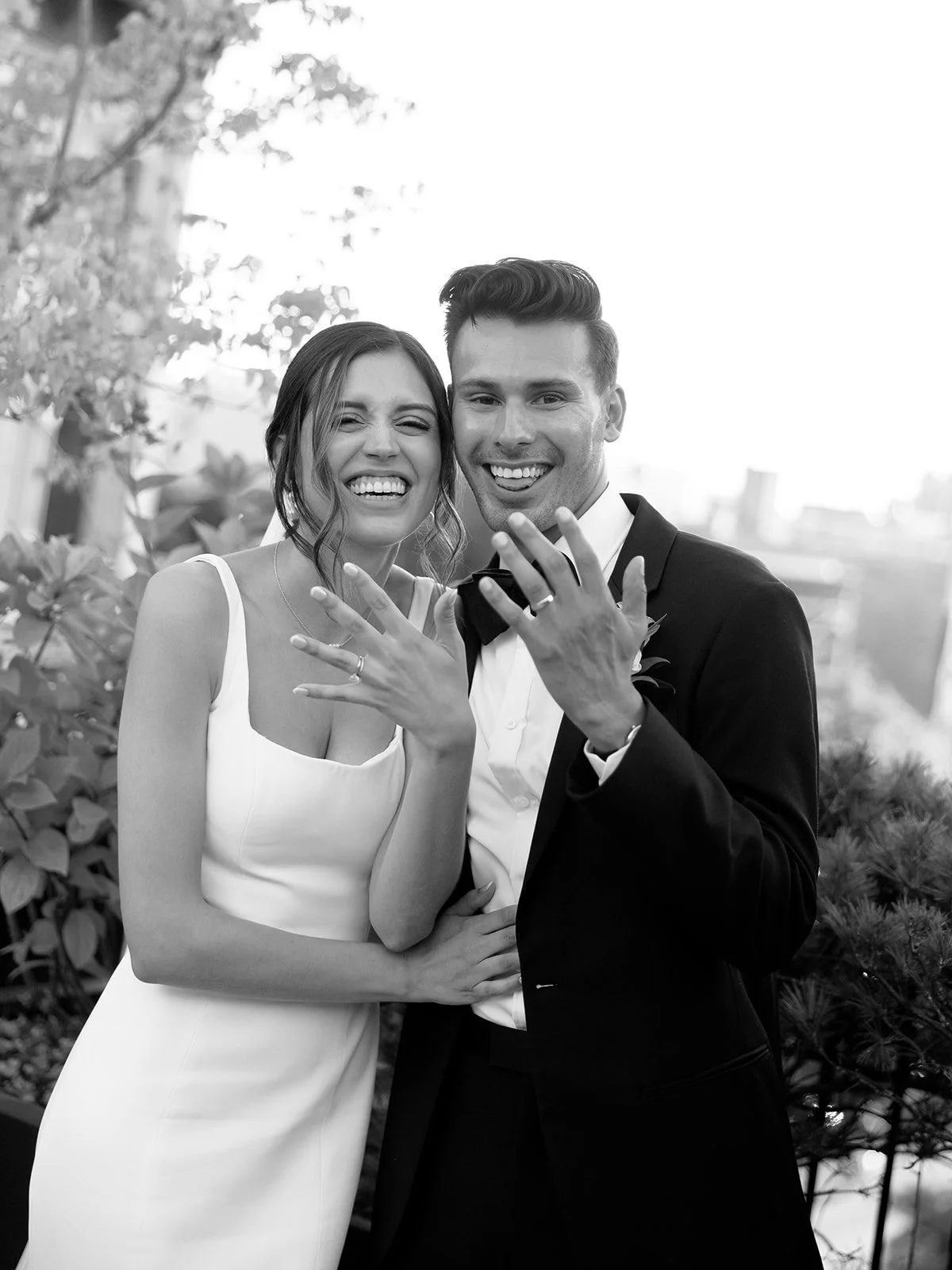 Black and white portrait of a laughing bride and groom showing off their wedding rings at Loft Lucia in Chicago, photographed by Chicago film wedding photographer Louie Abellera.