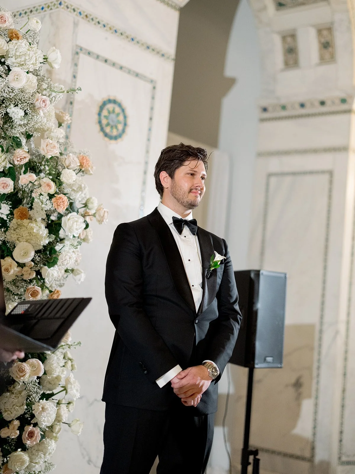 Brennan in formal black tie pose beside a tall white floral arrangement in Chicago Cultural Center. Shot on film by a Chicago wedding photographer.