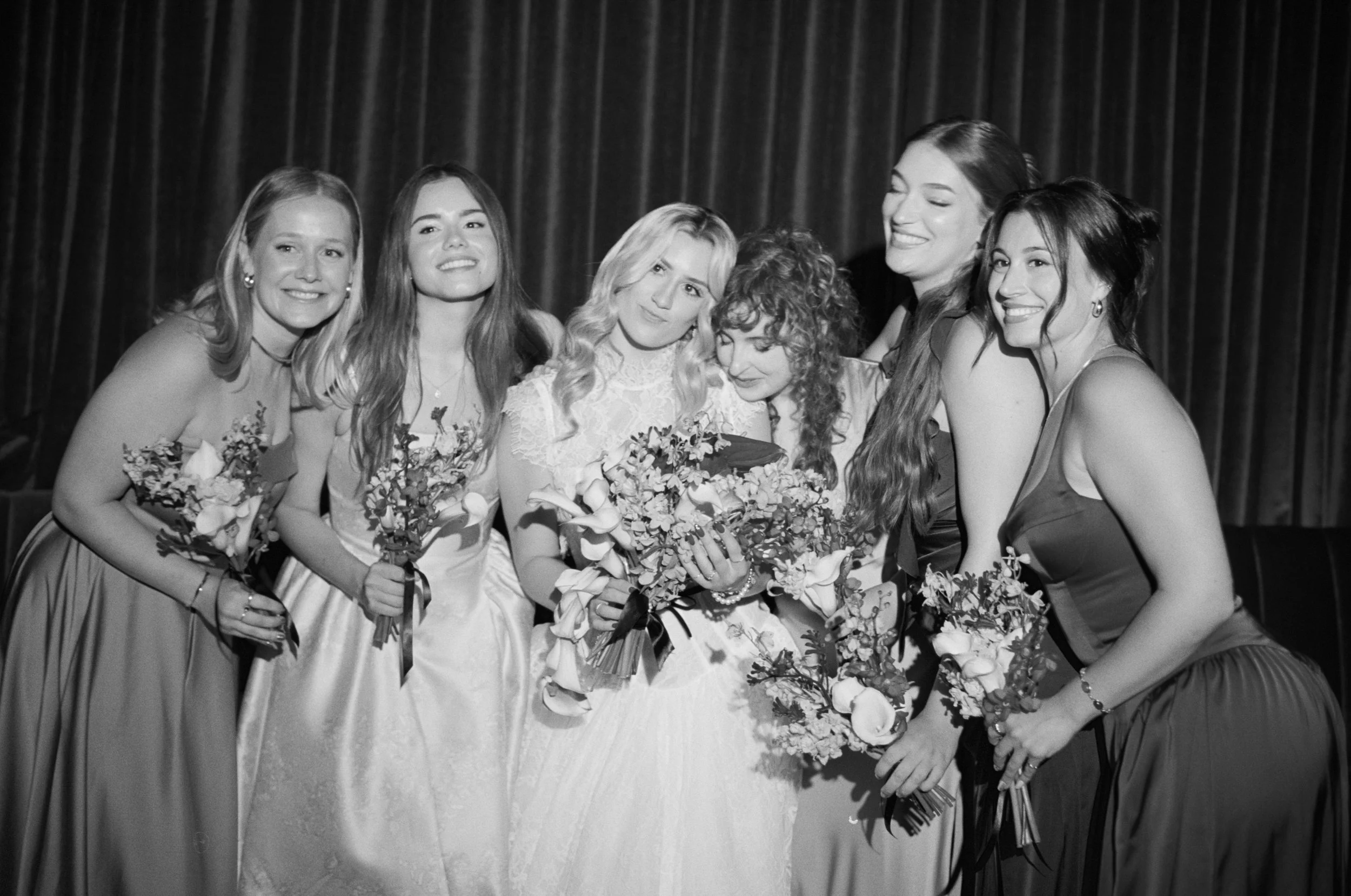 Black and white group portrait of the bridesmaids holding their bouquets inside The Wellsley's red velvet lounge