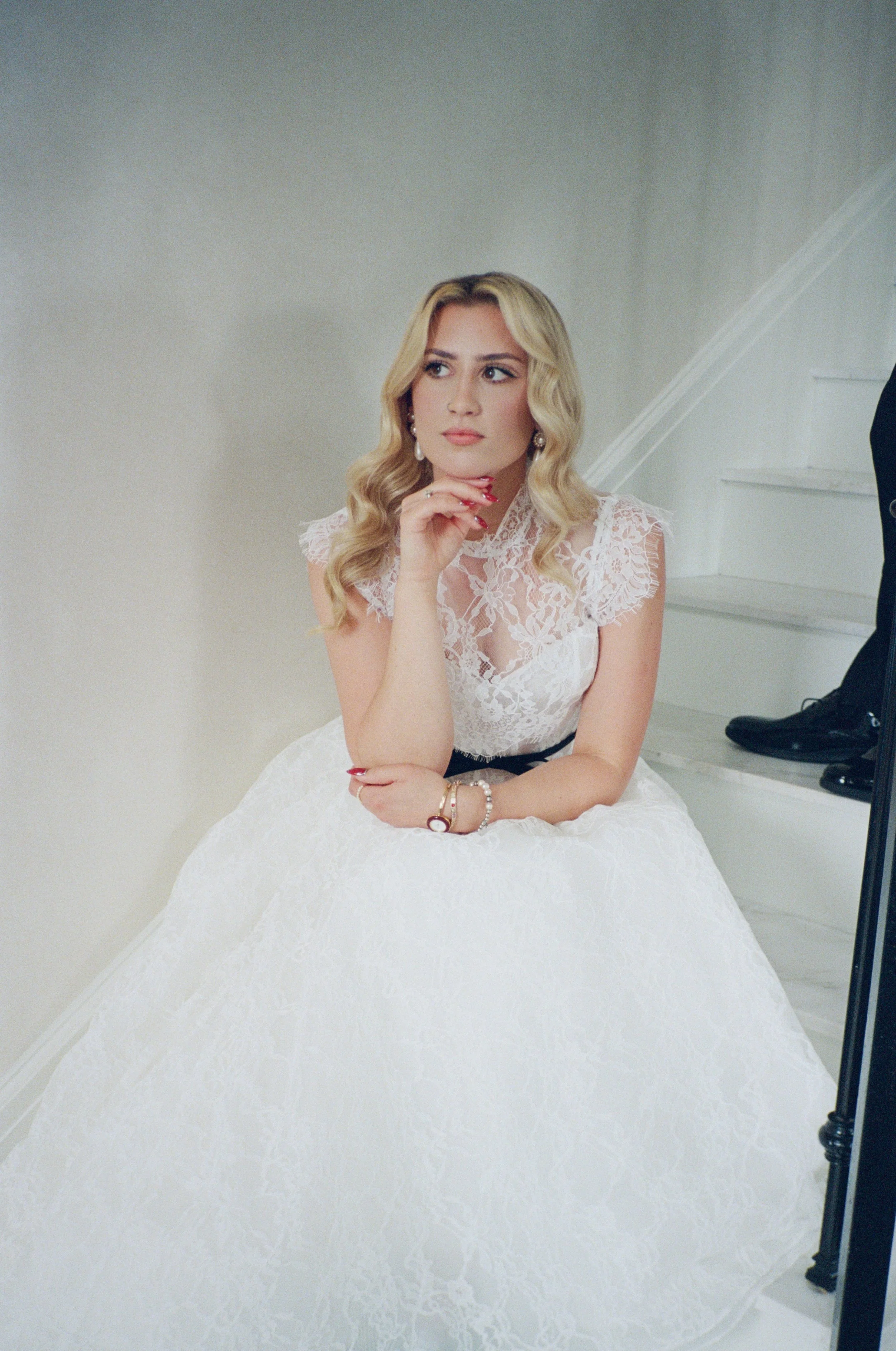 Bride sits quietly on the staircase in a contemplative portrait, chin resting on her hand