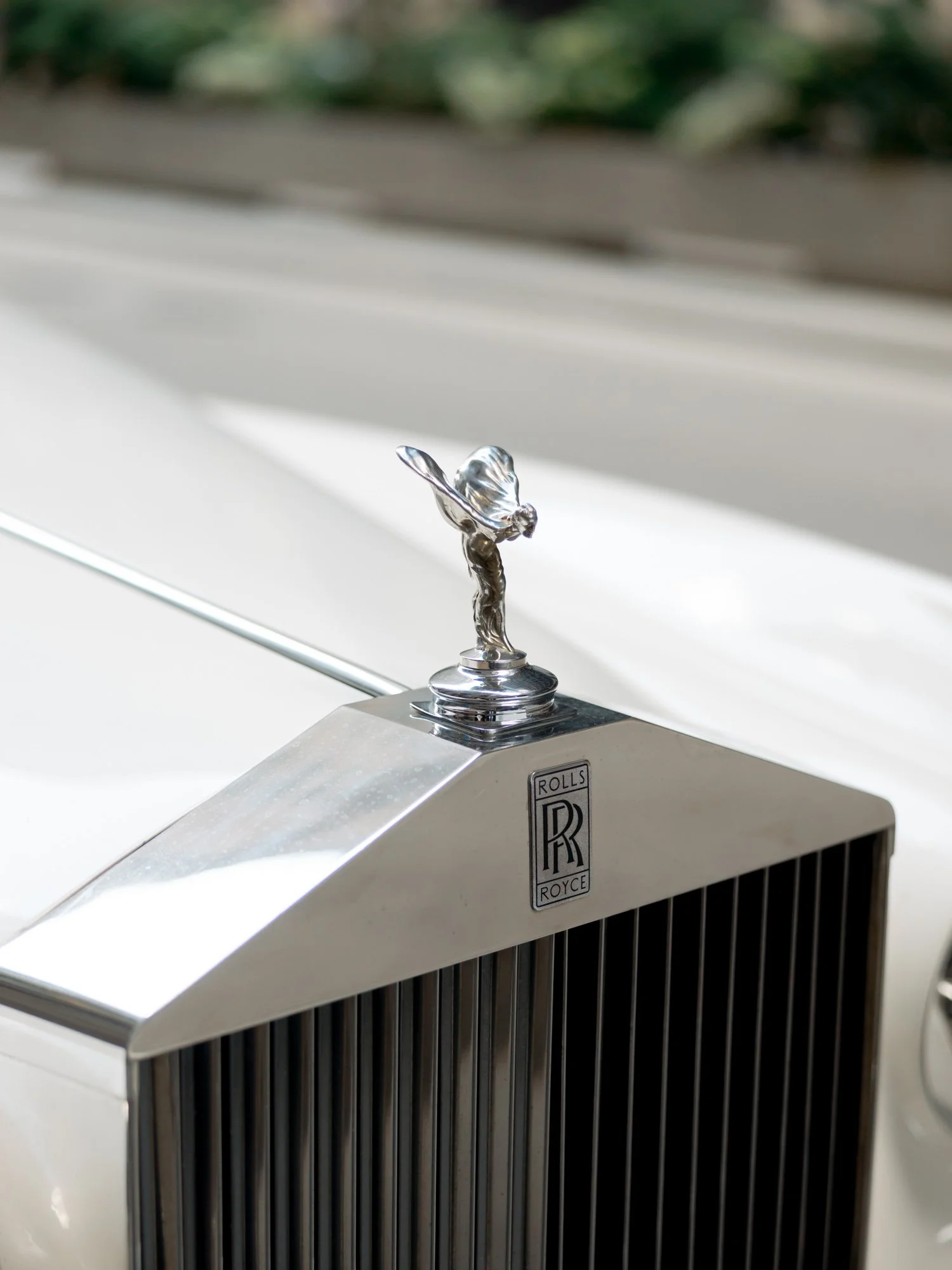 Close-up editorial detail of the Spirit of Ecstasy silver hood ornament on the vintage Rolls-Royce, sharp and gleaming — every detail was a decision.

