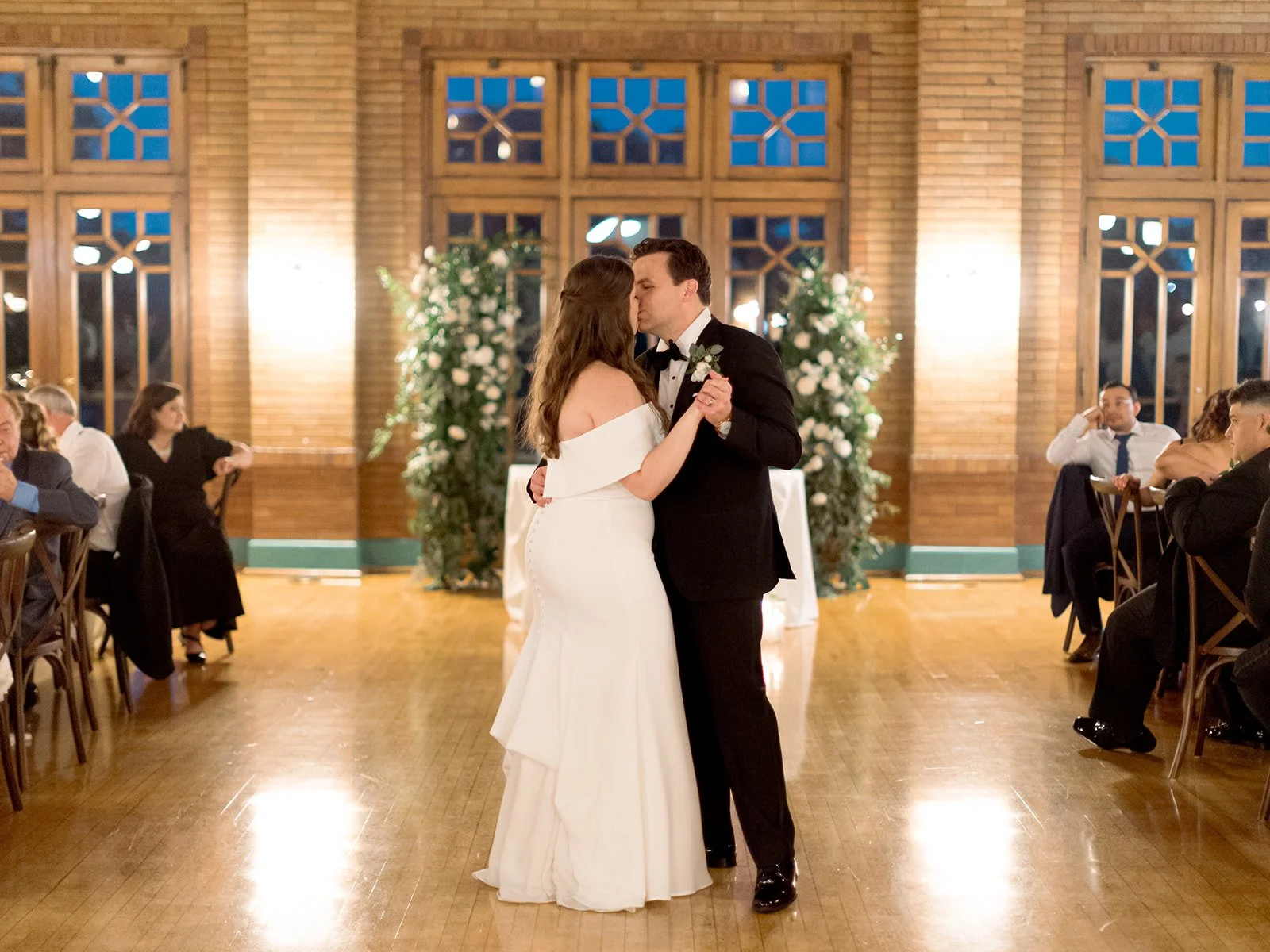 Lauren and Greg's first dance on the polished floor of Cafe Brauer's Great Hall in warm evening light, guests watching.