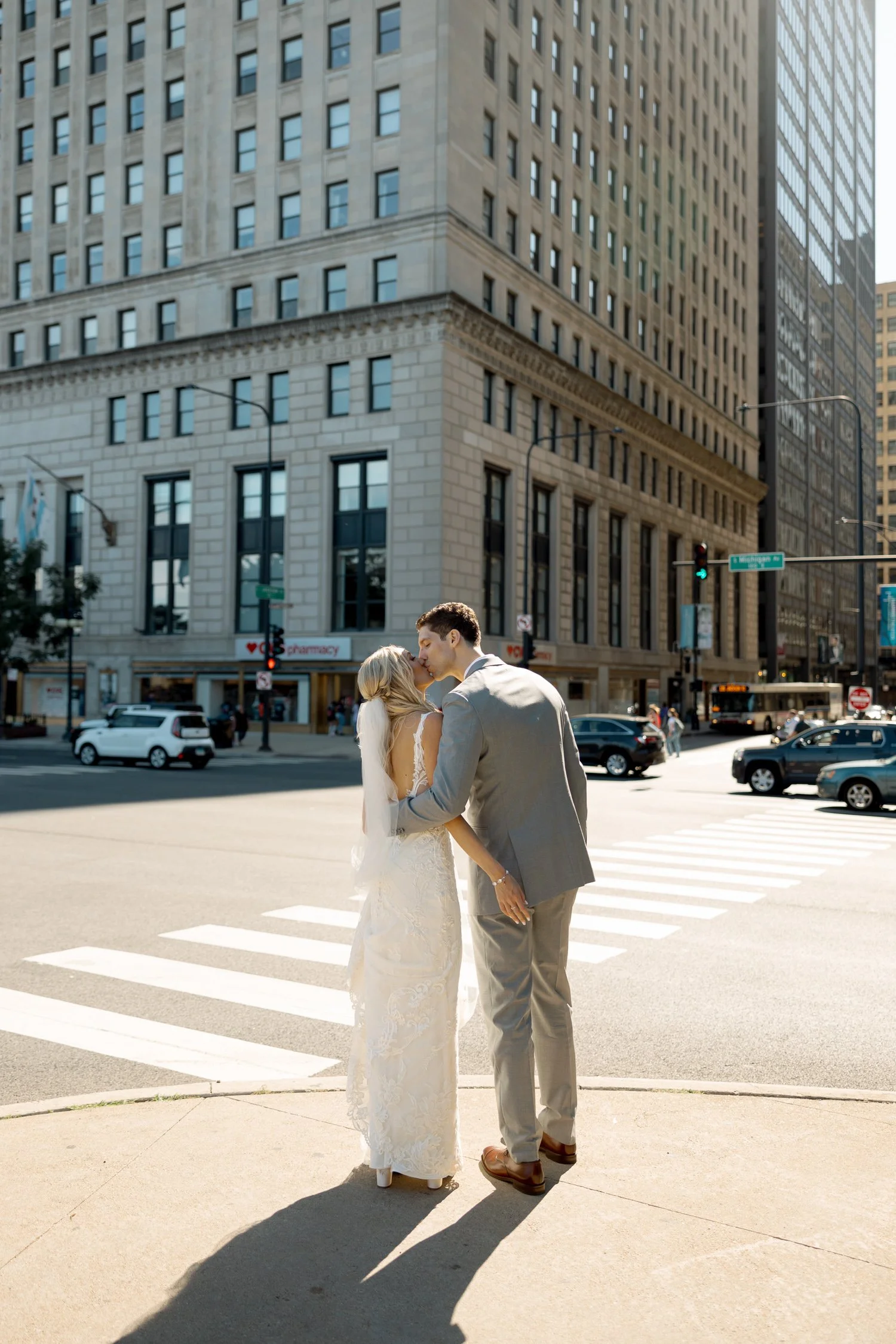 Bride and groom share a romantic kiss at a downtown Chicago street corner, tall city buildings framing their tender wedding day moment.