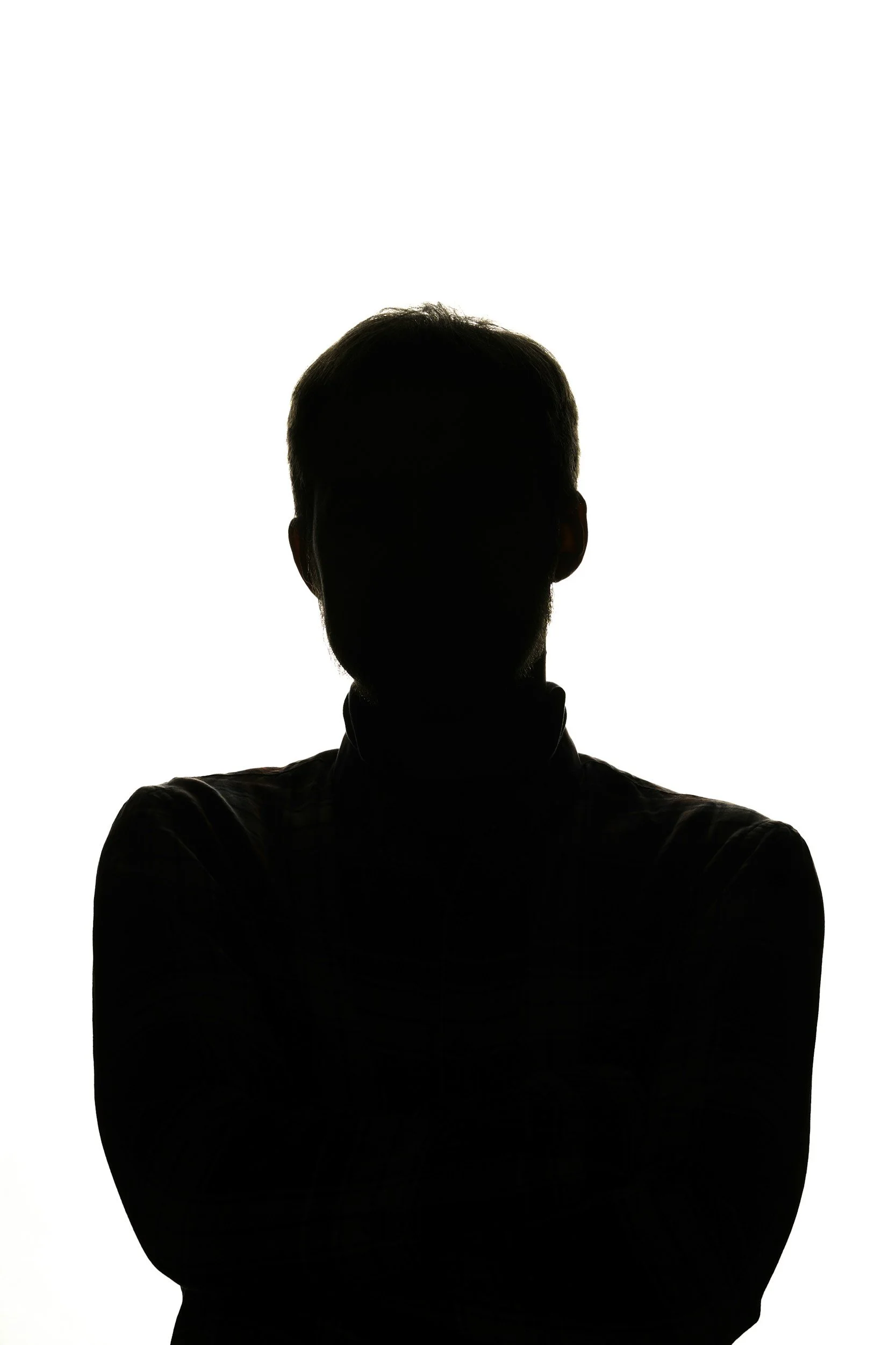 A silhouette of a person with short hair, seen against a bright white background, with arms crossed.