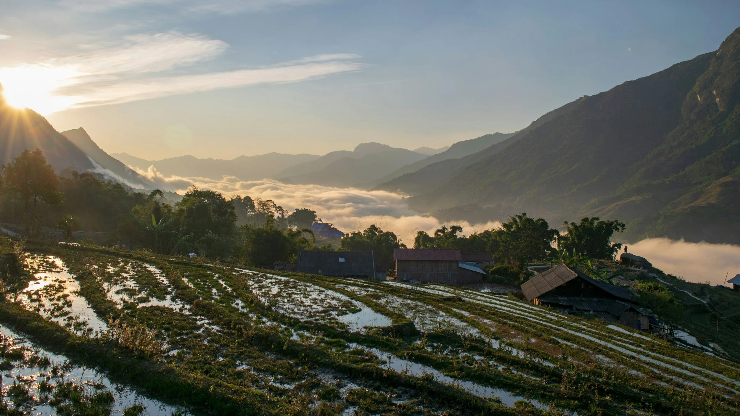 Sunrise over terraced rice fields and a mountain landscape with misty valleys and small rural houses.