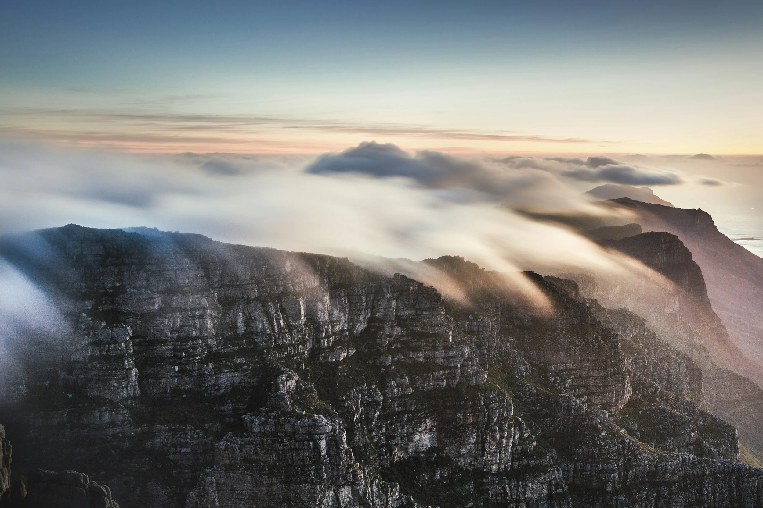 Soft clouds cascading over South Africa’s iconic mountain cliffs at dawn