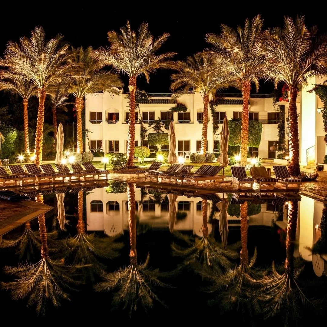 Palm-lined resort courtyard in Egypt at night, with softly lit architecture reflected in still water, creating a calm and private atmosphere.