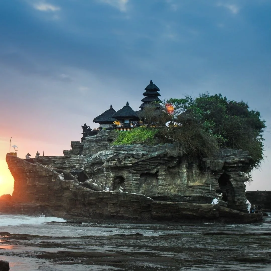 Tanah Lot sea temple in Bali set on a rocky coastal formation at sunset with waves and dramatic sky