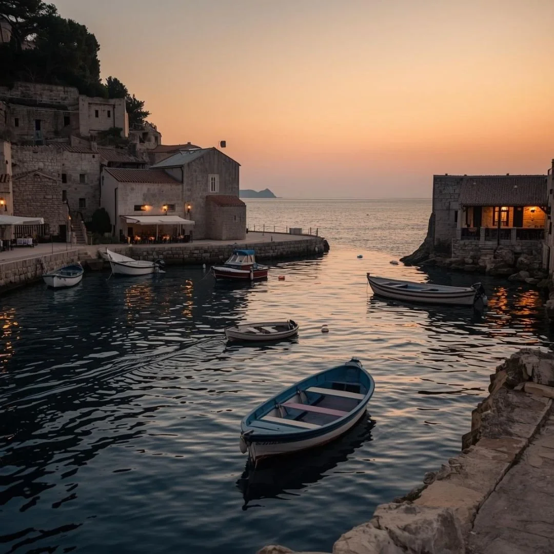 Small harbor on the Dalmatian Coast at sunset, with stone houses, moored boats, and calm Adriatic waters.
