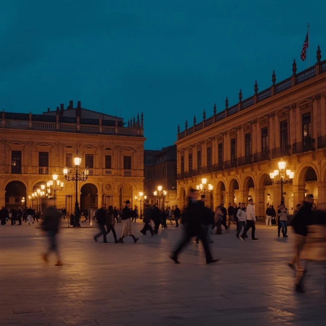 Evening in a grand Spanish plaza as warm streetlights glow against historic arcaded buildings, people moving through the square in soft motion, capturing the unhurried rhythm of city life after sunset.