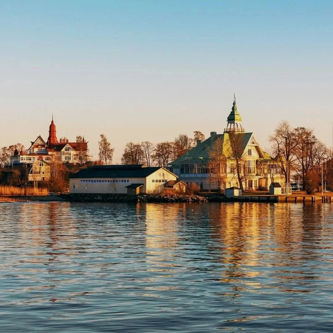 Historic waterfront buildings in Finland reflected in calm water under soft golden evening light.