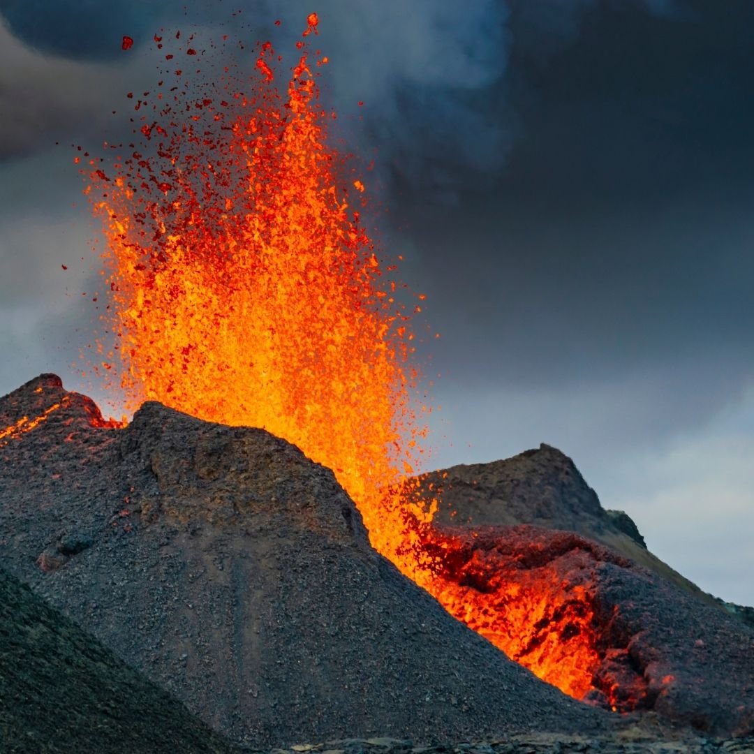 Active volcanic eruption in Iceland with molten lava bursting from a dark volcanic ridge under heavy clouds.