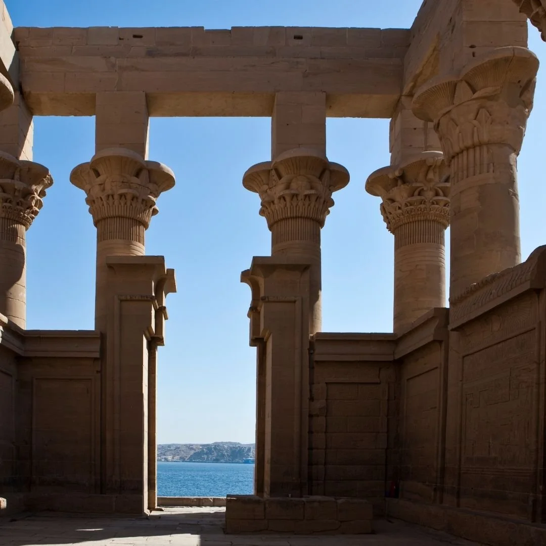 Stone columns of an ancient Egyptian temple in Aswan overlooking the Nile under a clear blue sky.