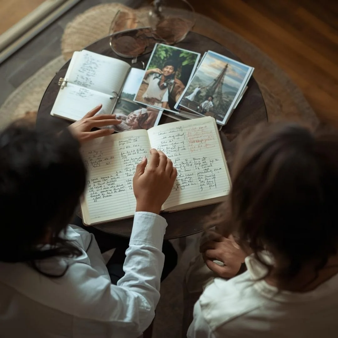Two adults reviewing a travel journal and photographs together, reflecting on experiences after a journey.