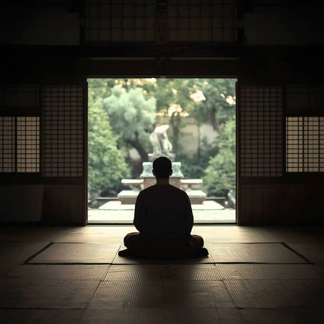 A person seated in quiet meditation inside a traditional Japanese temple, looking out onto a serene garden in soft morning light