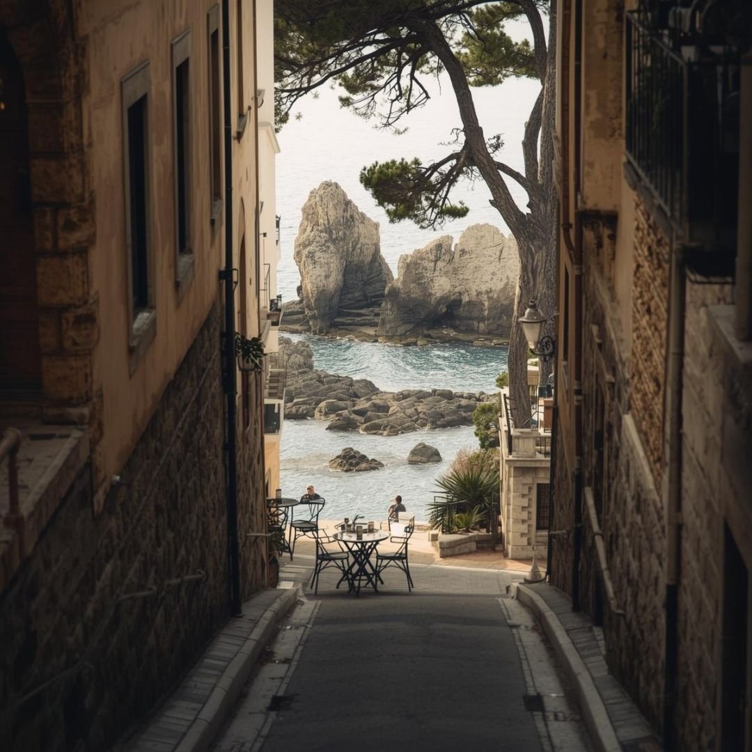 Narrow stone lane in Costa Brava opening toward a quiet rocky cove, with café tables set near the water, pine trees framing the sea, and calm Mediterranean light creating an unhurried, settled coastal atmosphere.
