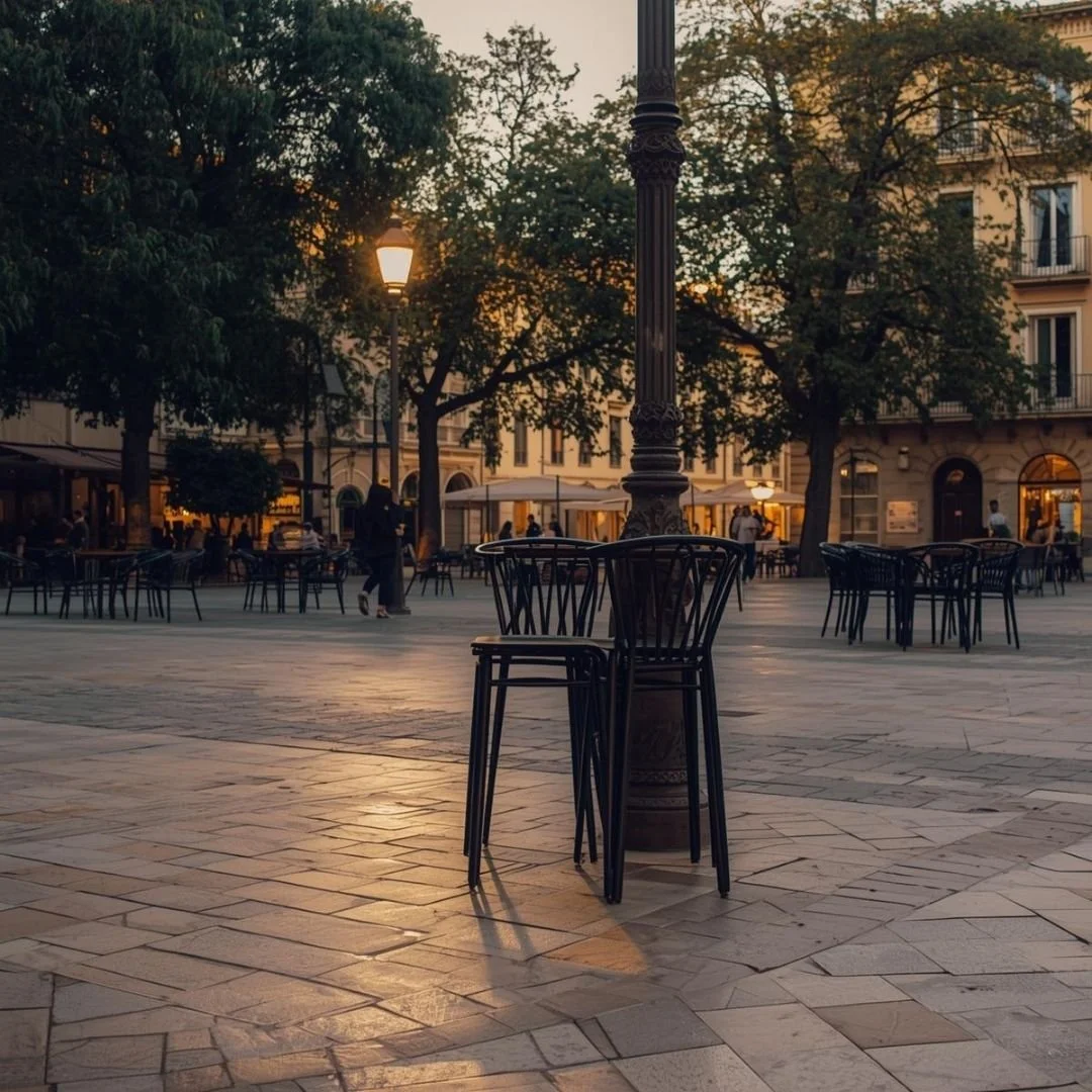 Quiet Spanish town square at dusk with café chairs, lampposts, and historic buildings under soft evening light.