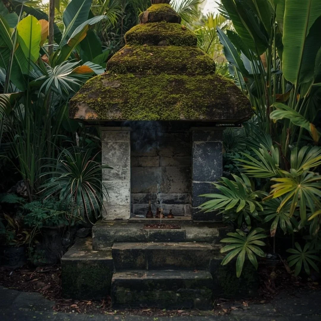Moss-covered Balinese stone shrine surrounded by tropical greenery with incense gently rising in a quiet garden setting