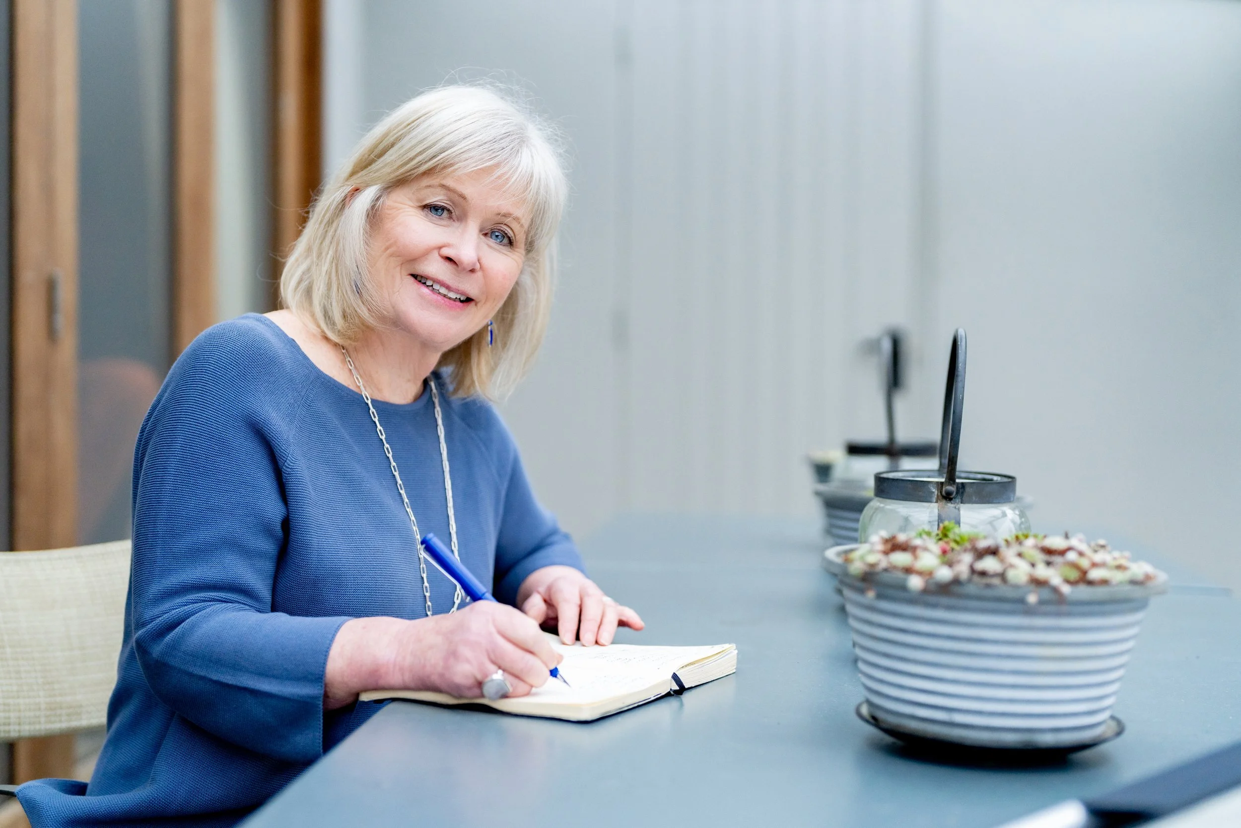 Heartwood Stories owner writes in notebook as she smiles at the camera