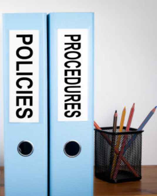 Two blue binders labeled 'POLICIES' and 'PROCEDURES' placed on a desk next to a black pencil holder with colored pencils.