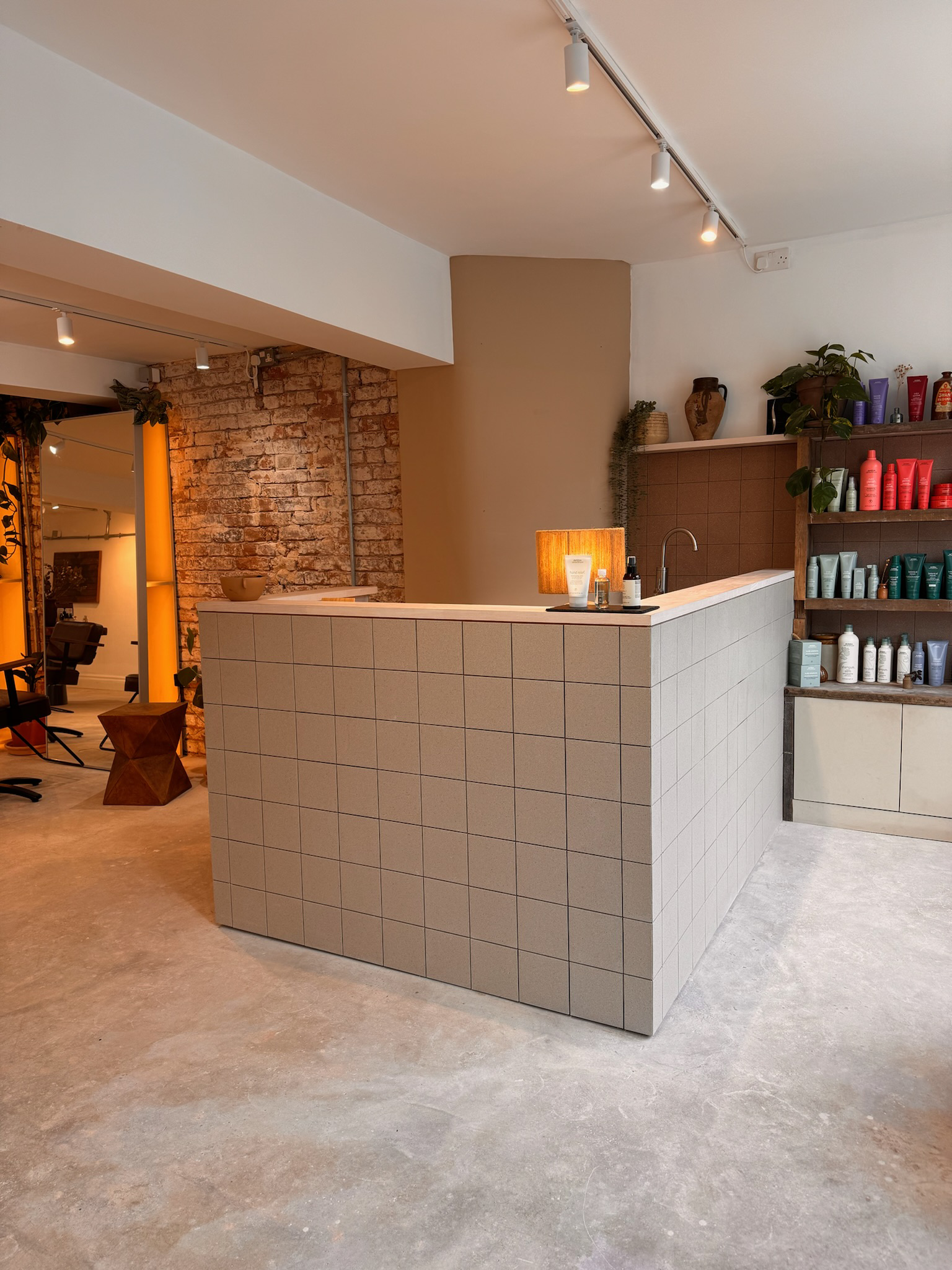 Modern salon reception desk with tiles, shelves with hair products, and a small sink area in a stylish interior.