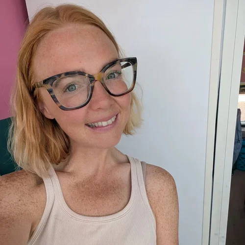 A woman with red hair, glasses, and freckles smiling for a selfie.