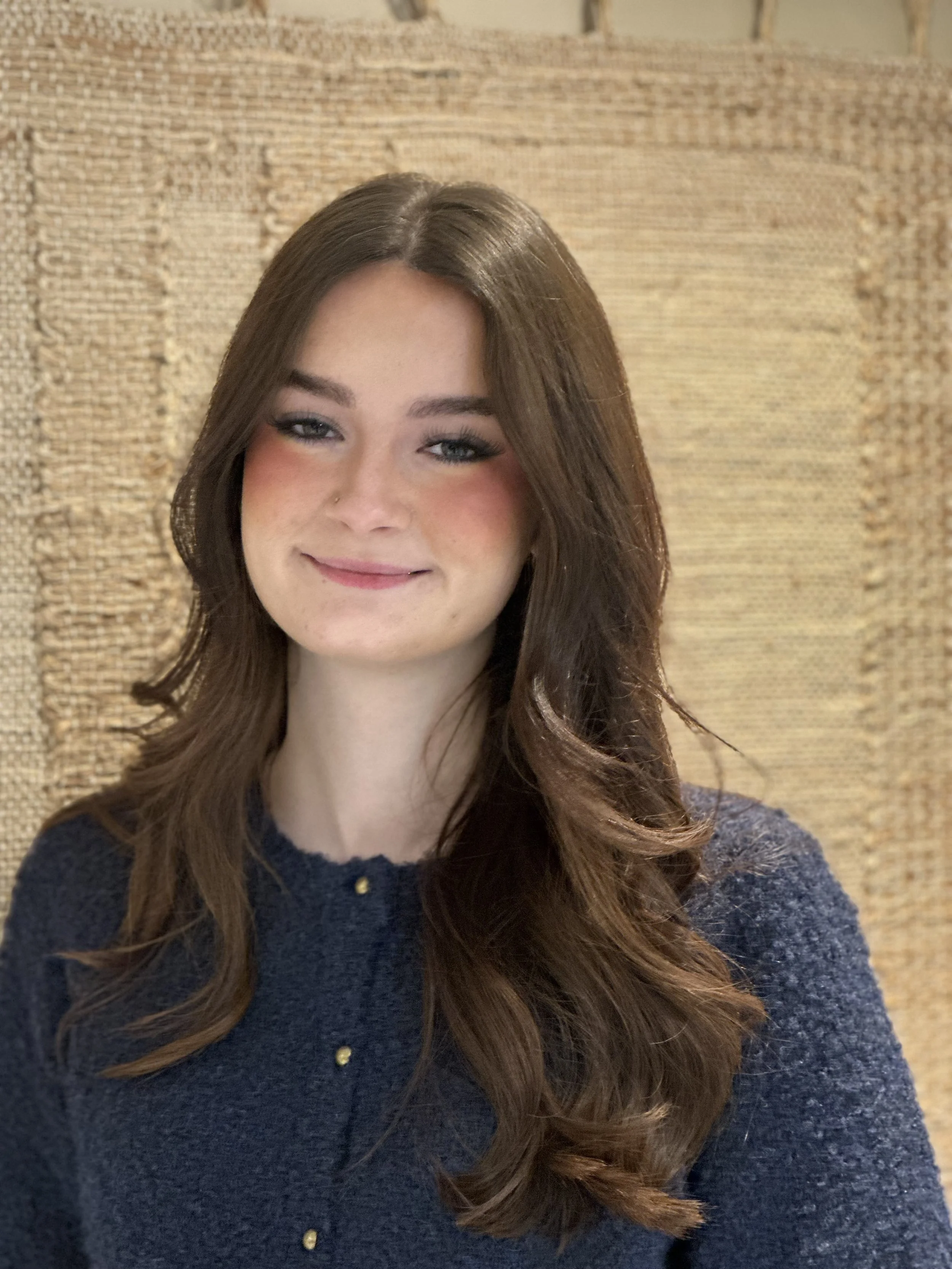 Sophia, trainee stylist at Butchers hair salon chester in front of a beige wall hanging