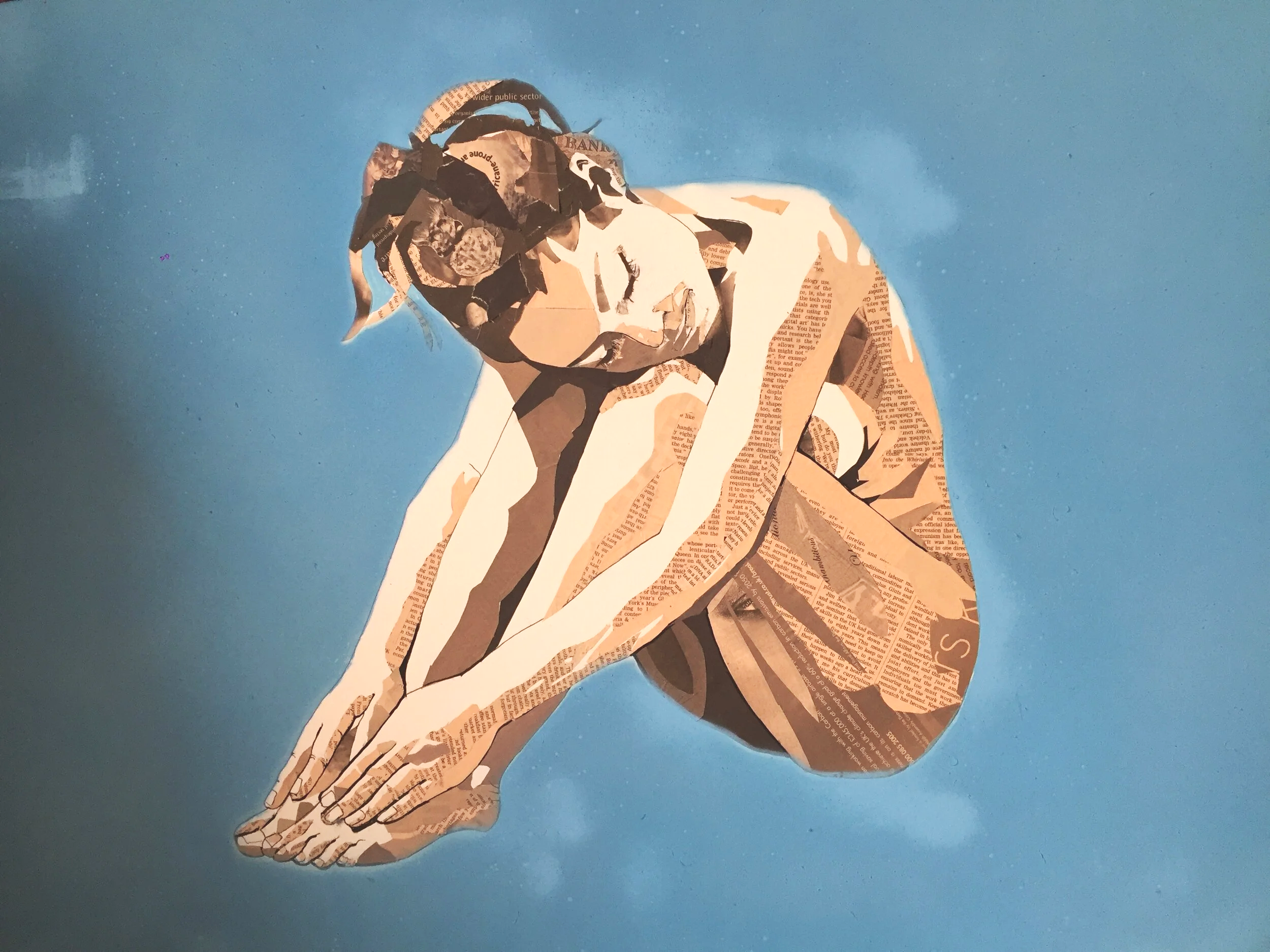 Collage artwork of a woman sitting with knees drawn up, composed of torn newspaper and magazine clippings on a blue background.