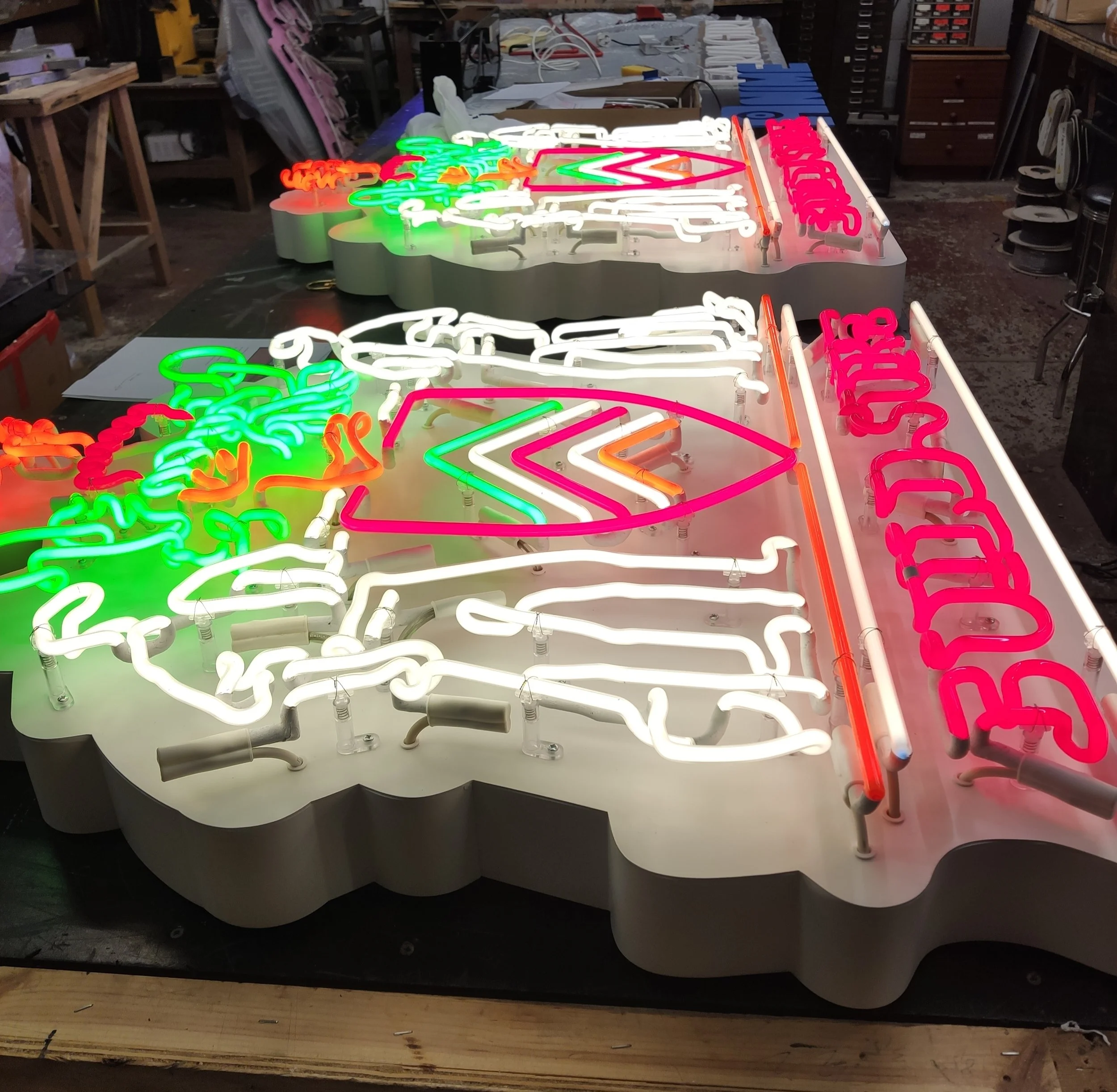 Colorful neon sign with various letters and designs, placed on a work table in a workshop setting.