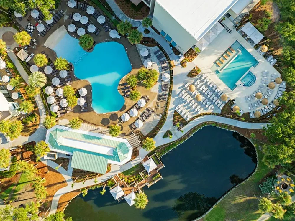 Aerial view of a luxurious resort with a swimming pool, a hot tub, a pond, and surrounding lush greenery.