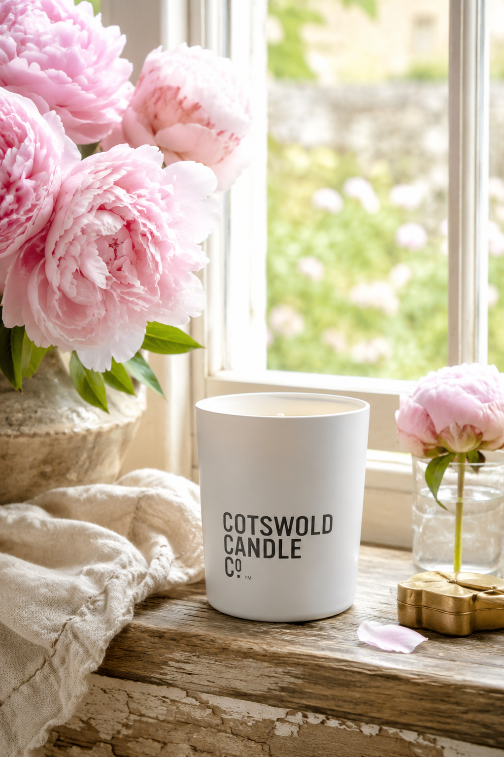 Cotswold Candle Co. Peony scented candle styled on a summer windowsill with fresh pink peonies