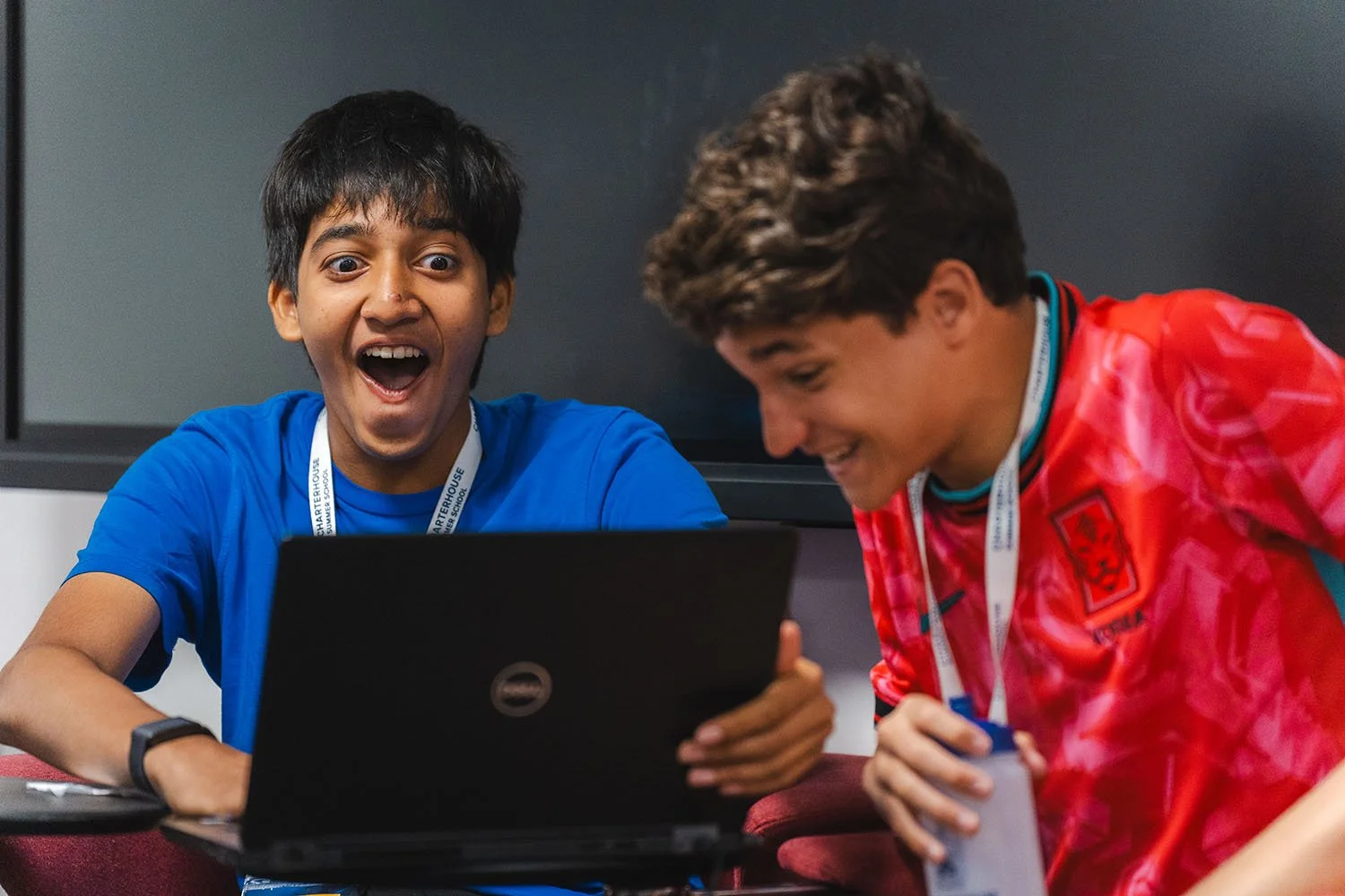 Two students laughing over laptop in robotics class